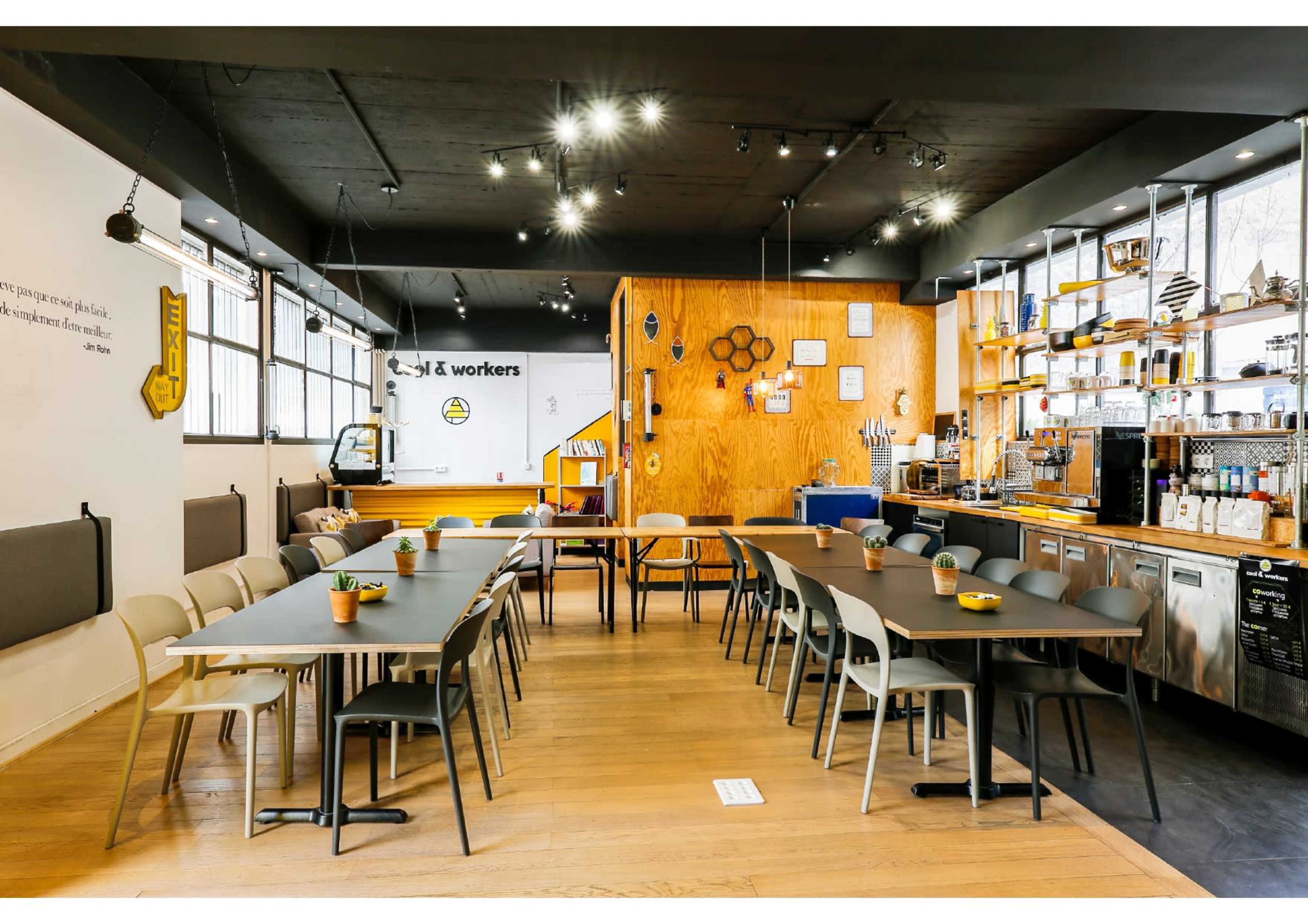 A modern café interior with wooden accents, long tables arranged in a communal setting, and a well-stocked beverage counter.