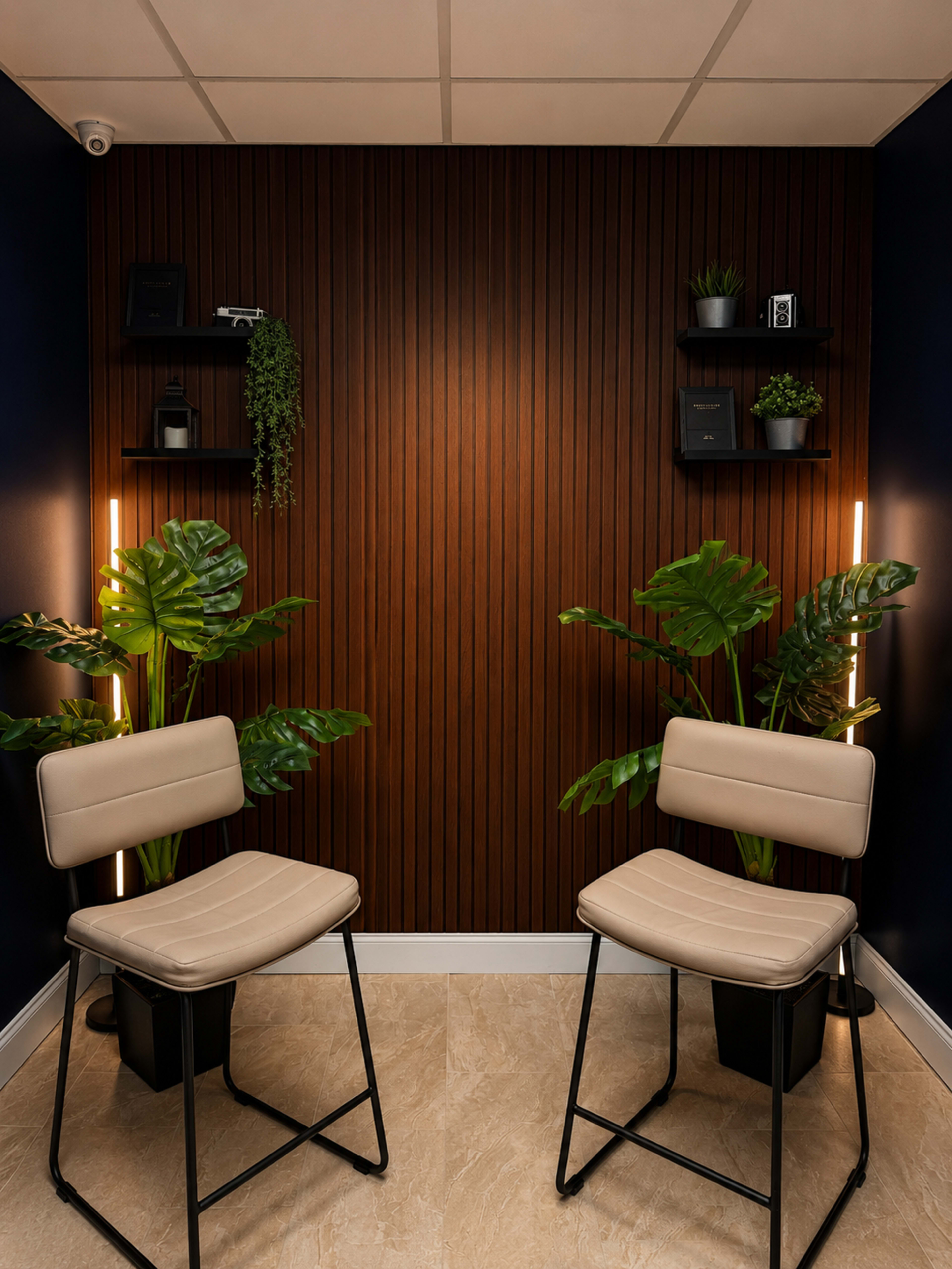 The image shows a small, modern space with two cream-colored chairs facing a wooden wall adorned with shelves holding plants and decorative items.