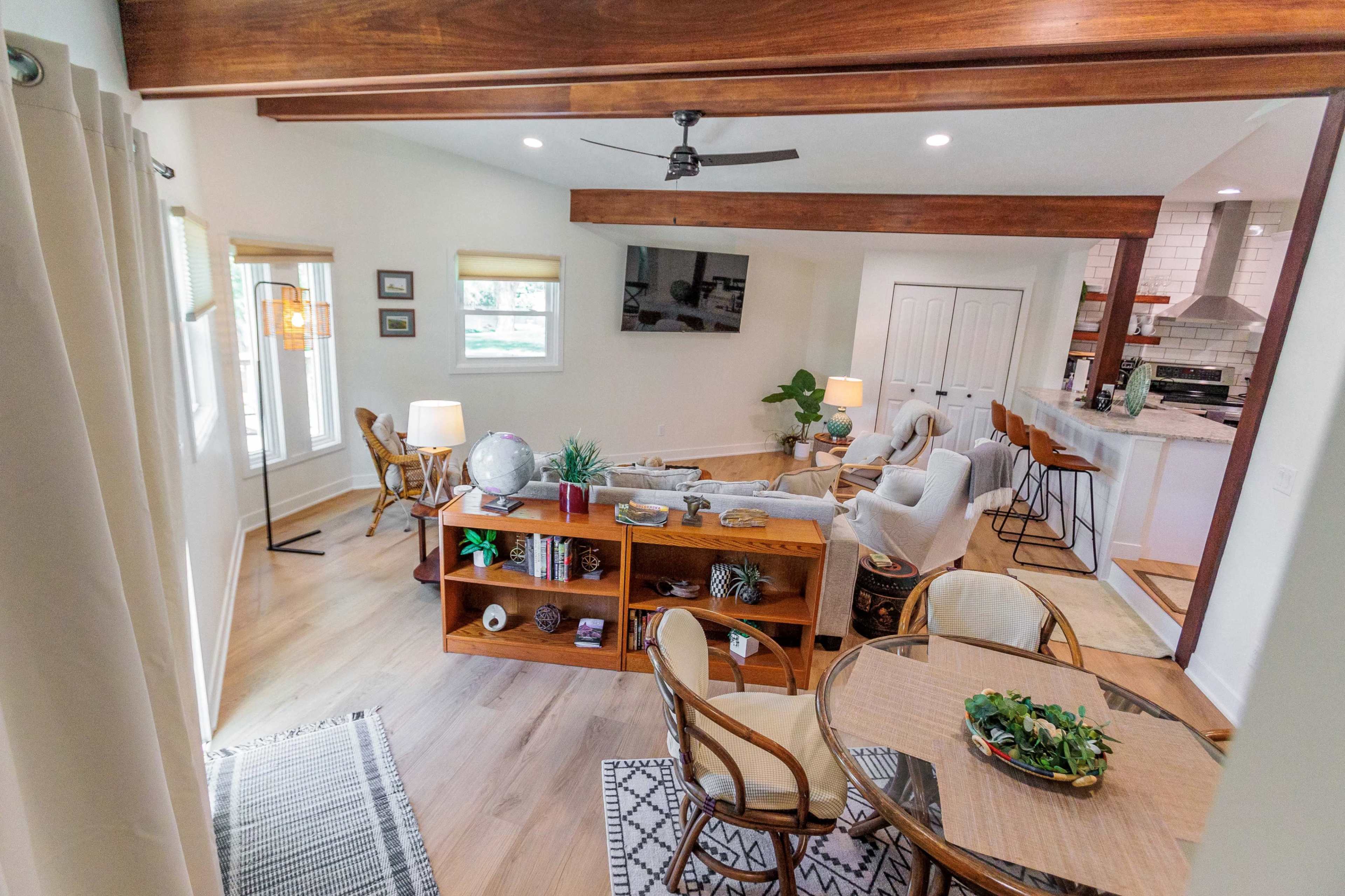 The image shows a modern, open-concept living area with a seating arrangement, a dining table, and a kitchen in the background.