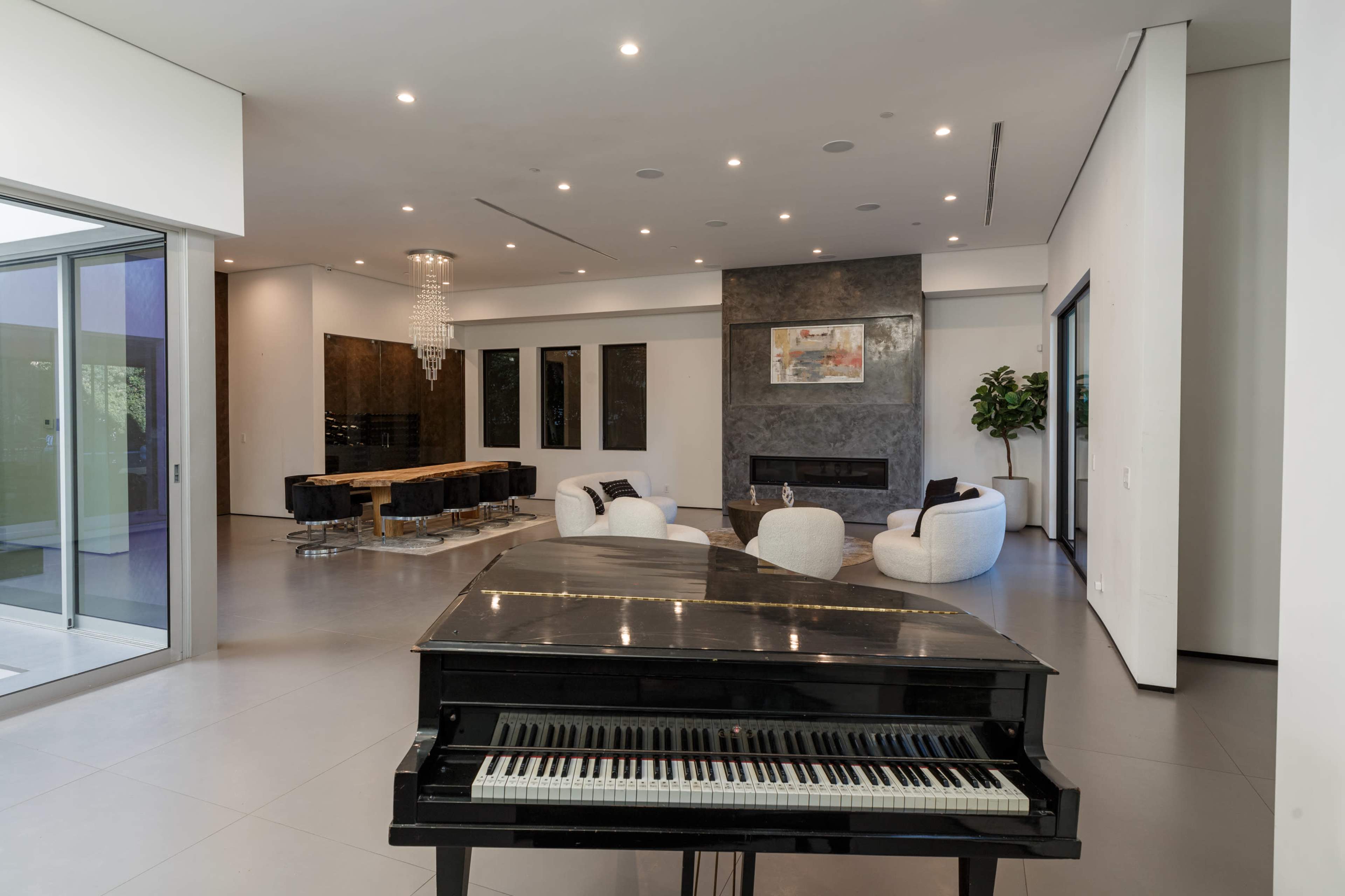 A black piano sits in a modern open-concept living space featuring a dining area and a fireplace.