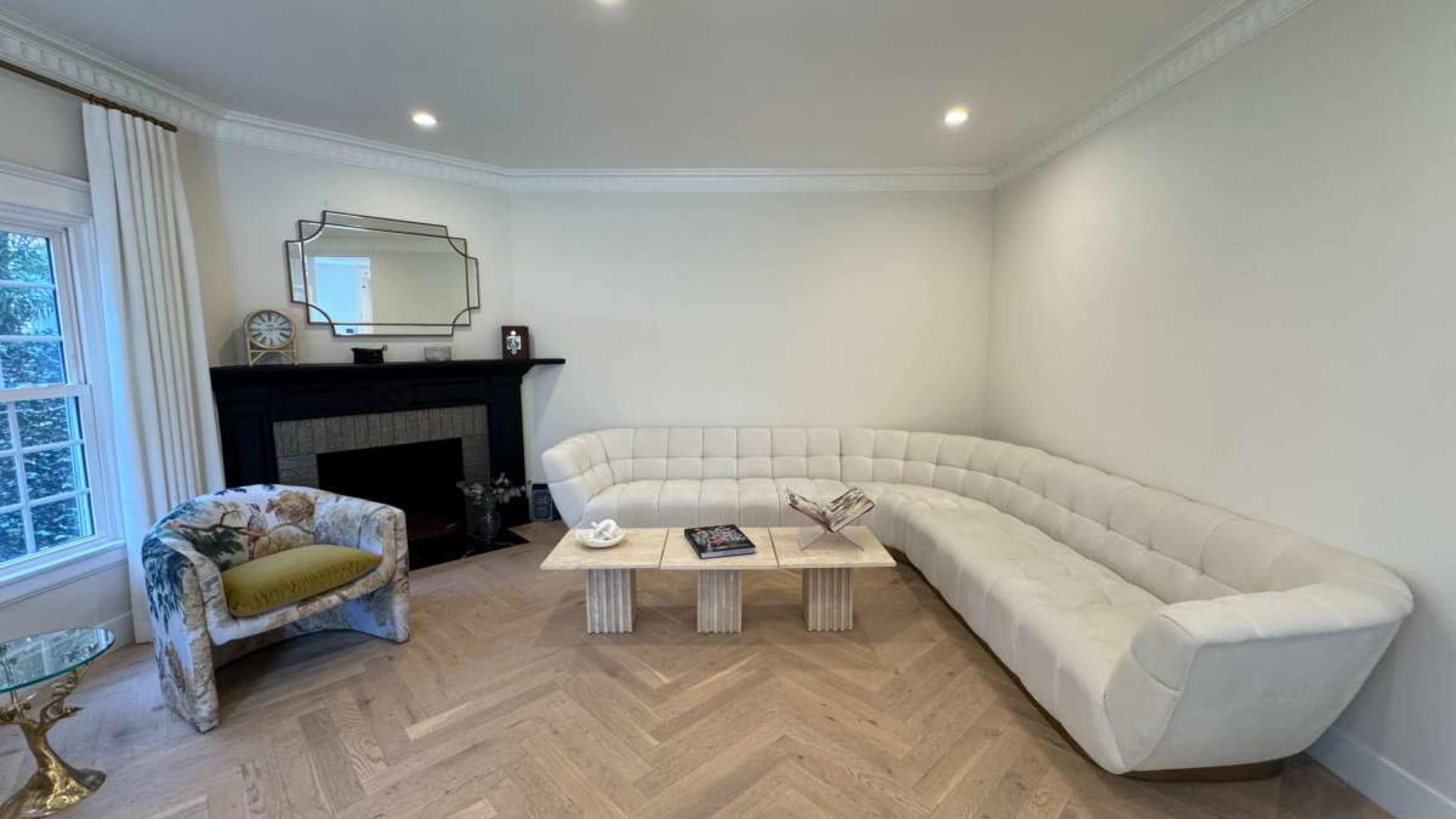The image shows a modern living room featuring a curved white sofa, a light wood coffee table, and a decorative armchair in a corner.
