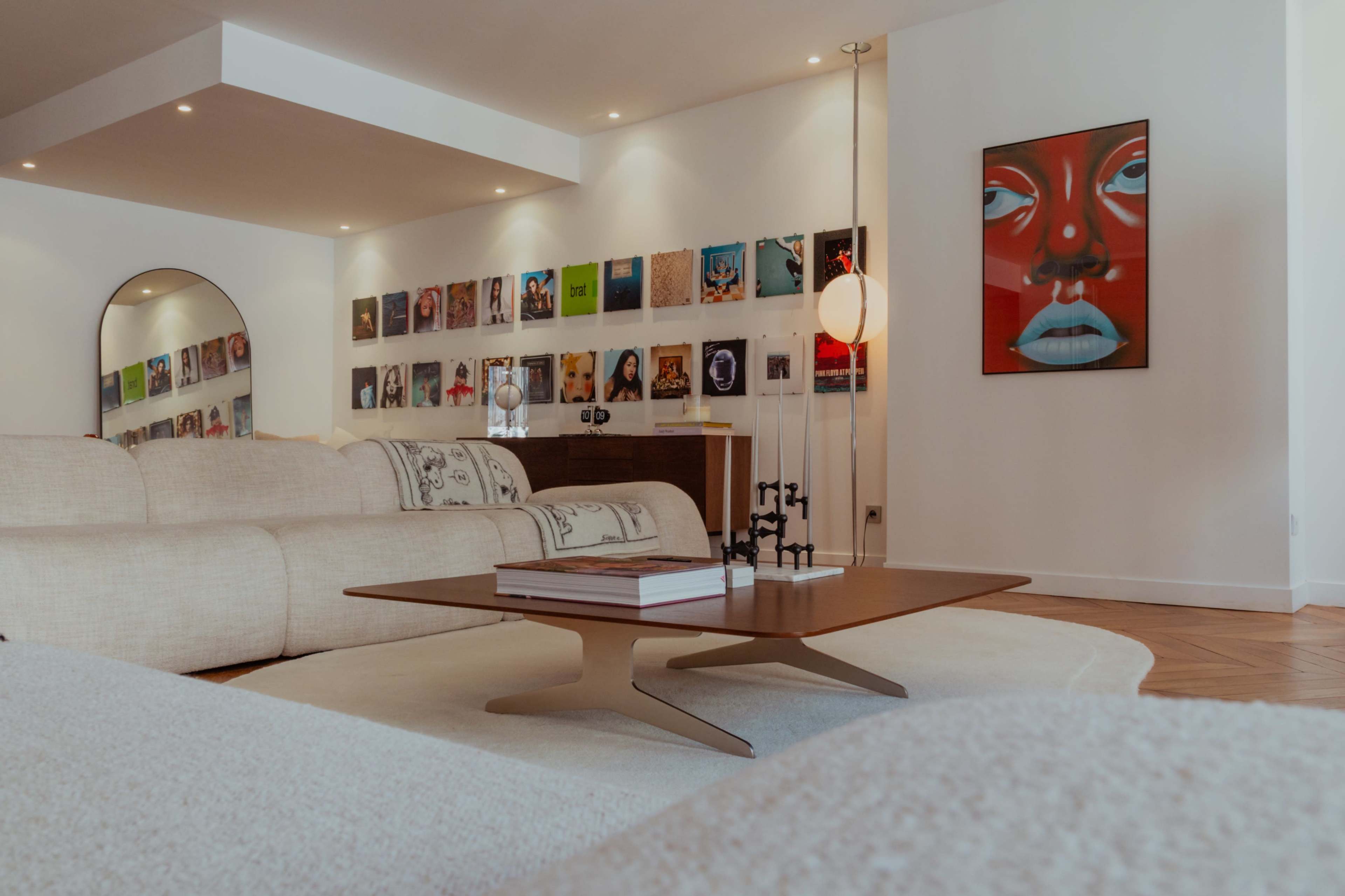 A spacious living room features a beige sofa, a coffee table, and a wall adorned with framed vinyl records and a colorful artwork.
