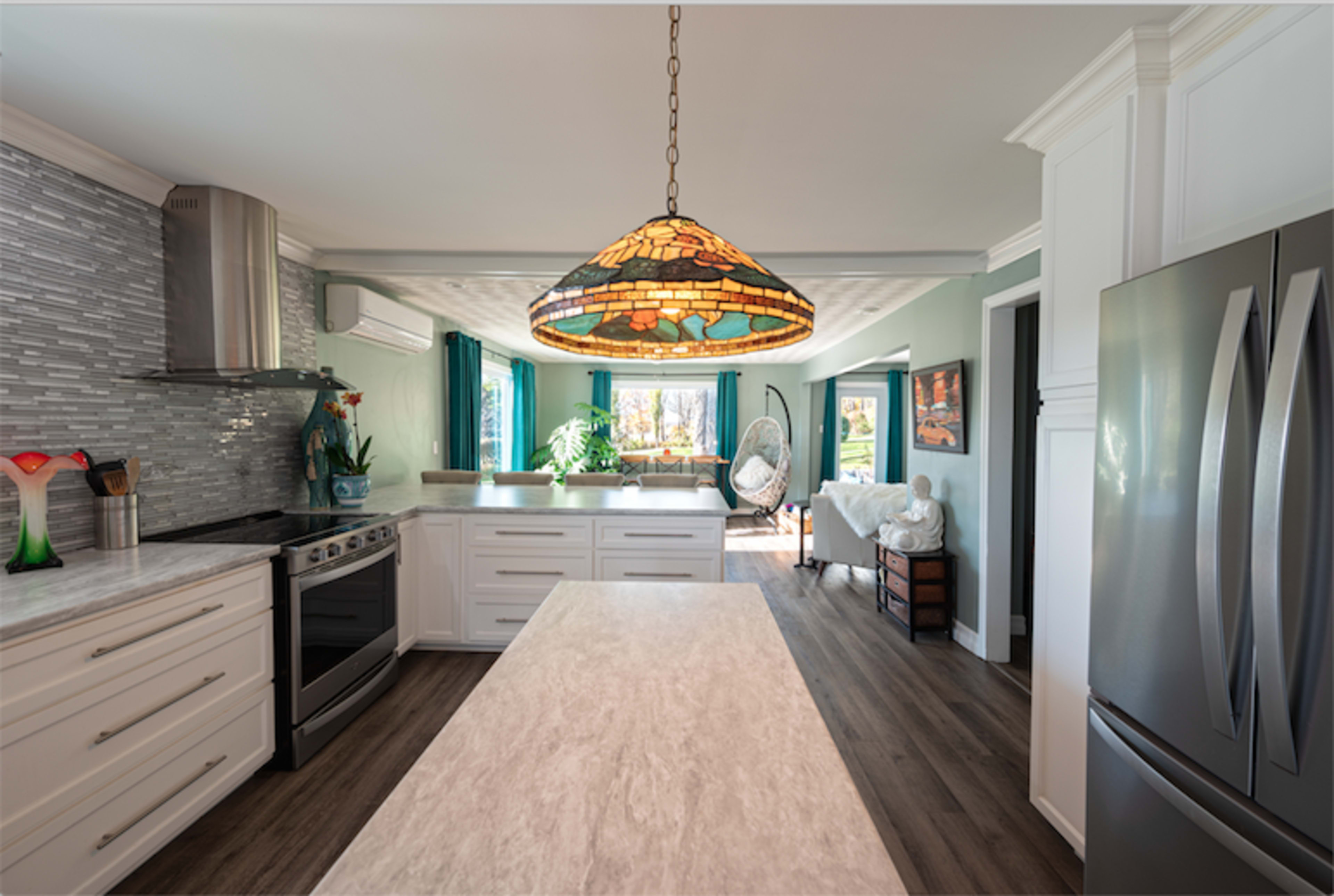 A modern kitchen features a large island with a marble countertop, stainless steel appliances, and a stained glass pendant light.