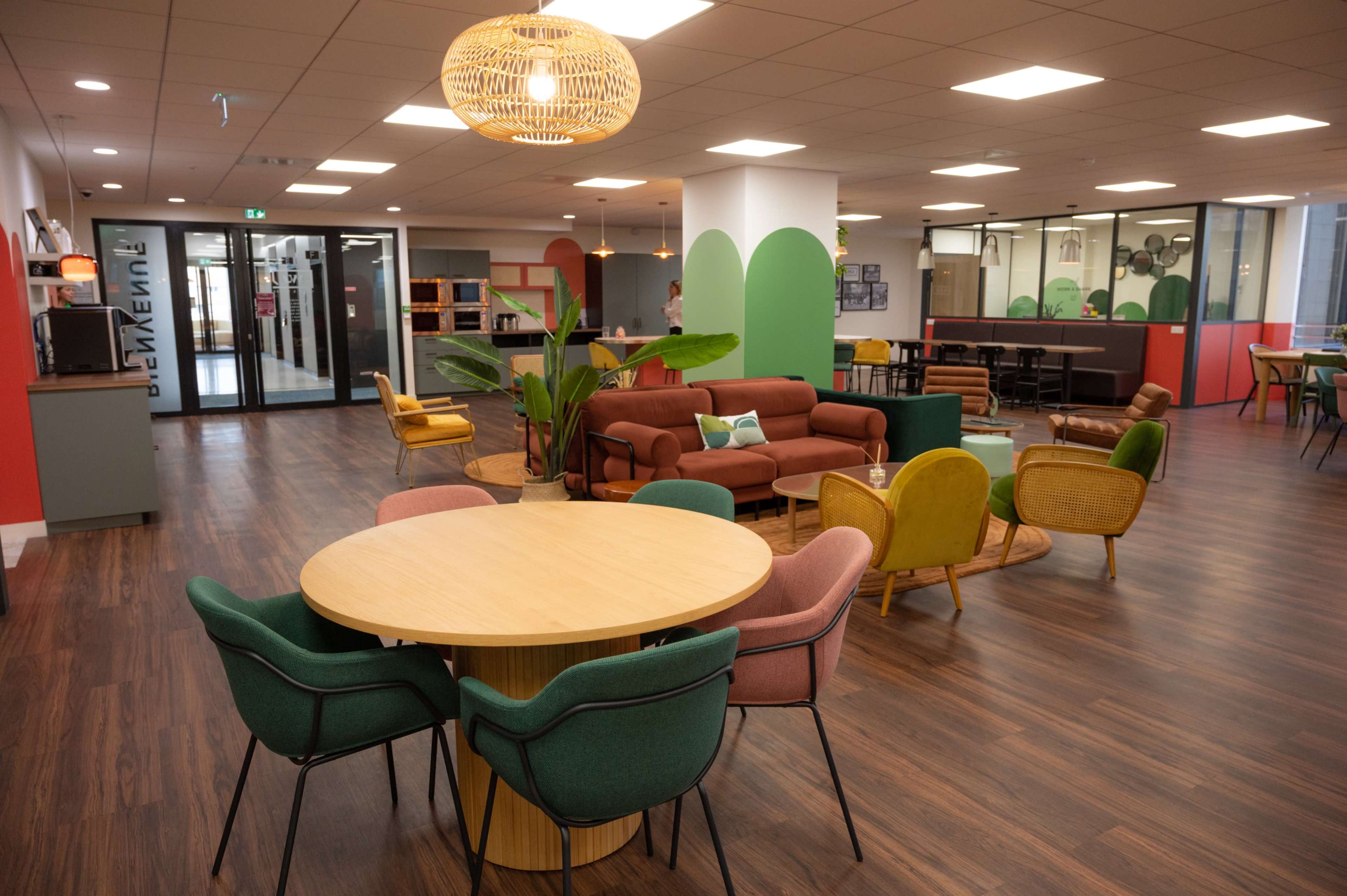 A modern, open office lounge featuring various seating arrangements, a round wooden table, and decorations on the walls.