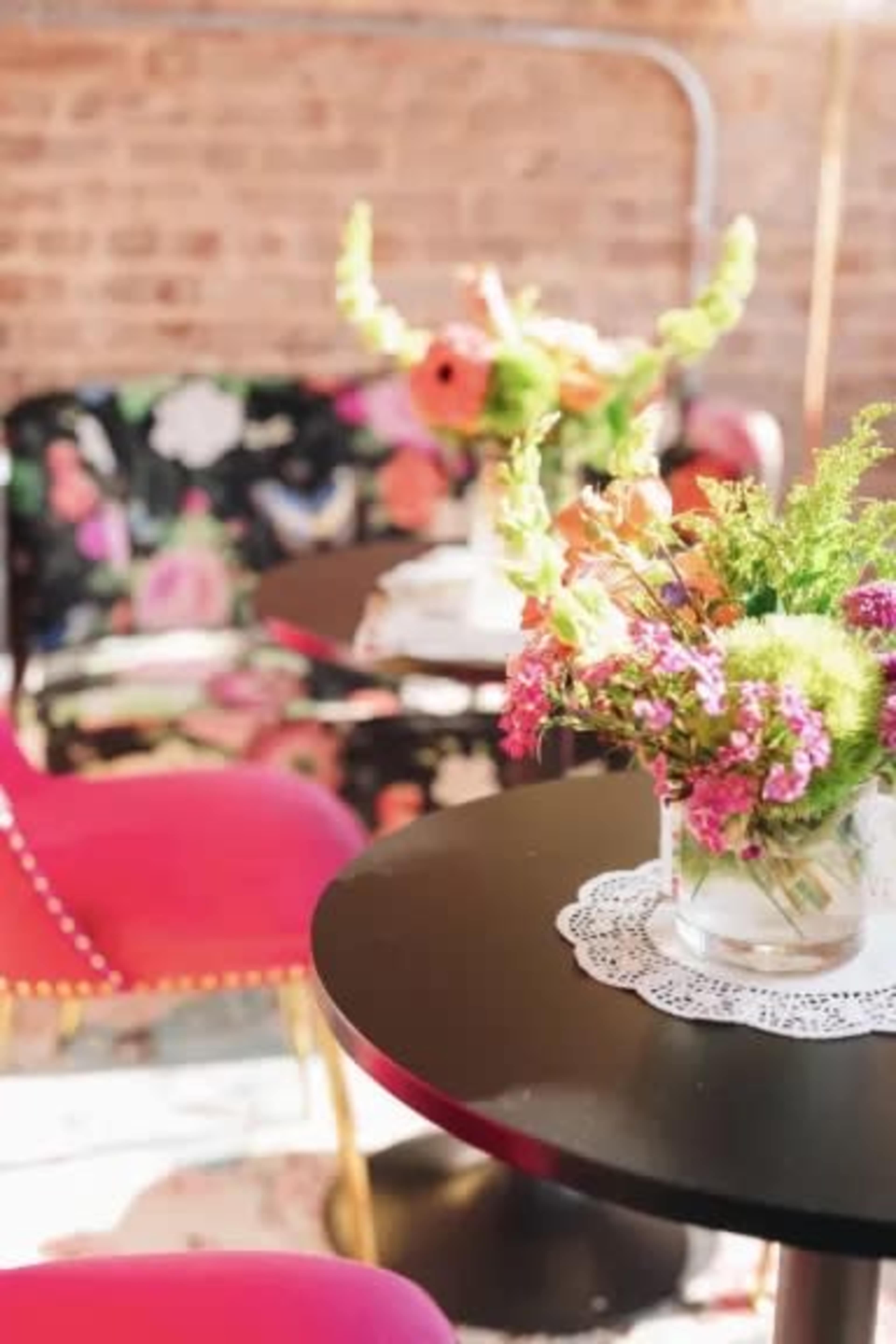 A brightly decorated café features a floral sofa and tables adorned with vibrant floral arrangements.