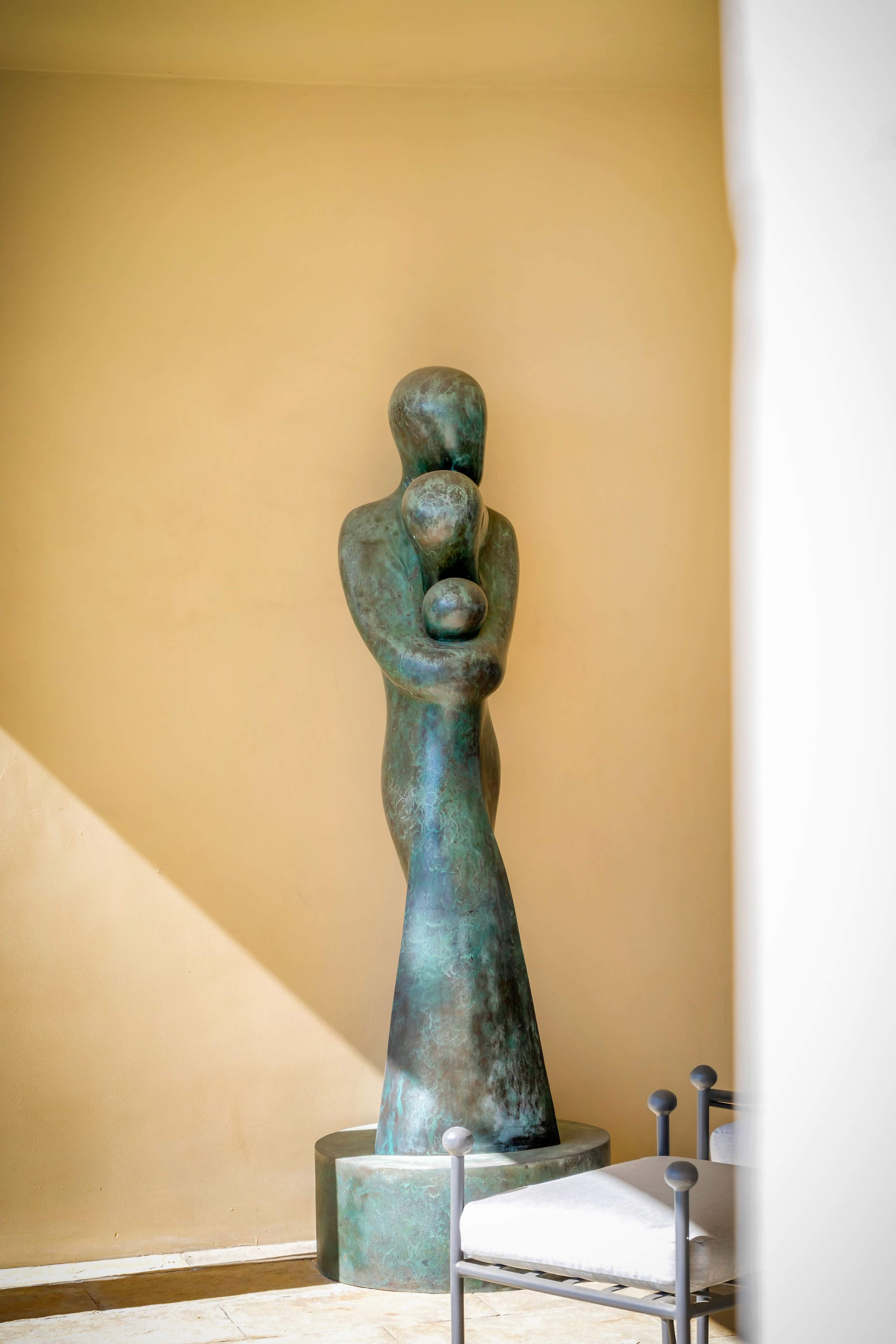 A bronze statue of a figure holding a child stands against a beige wall.