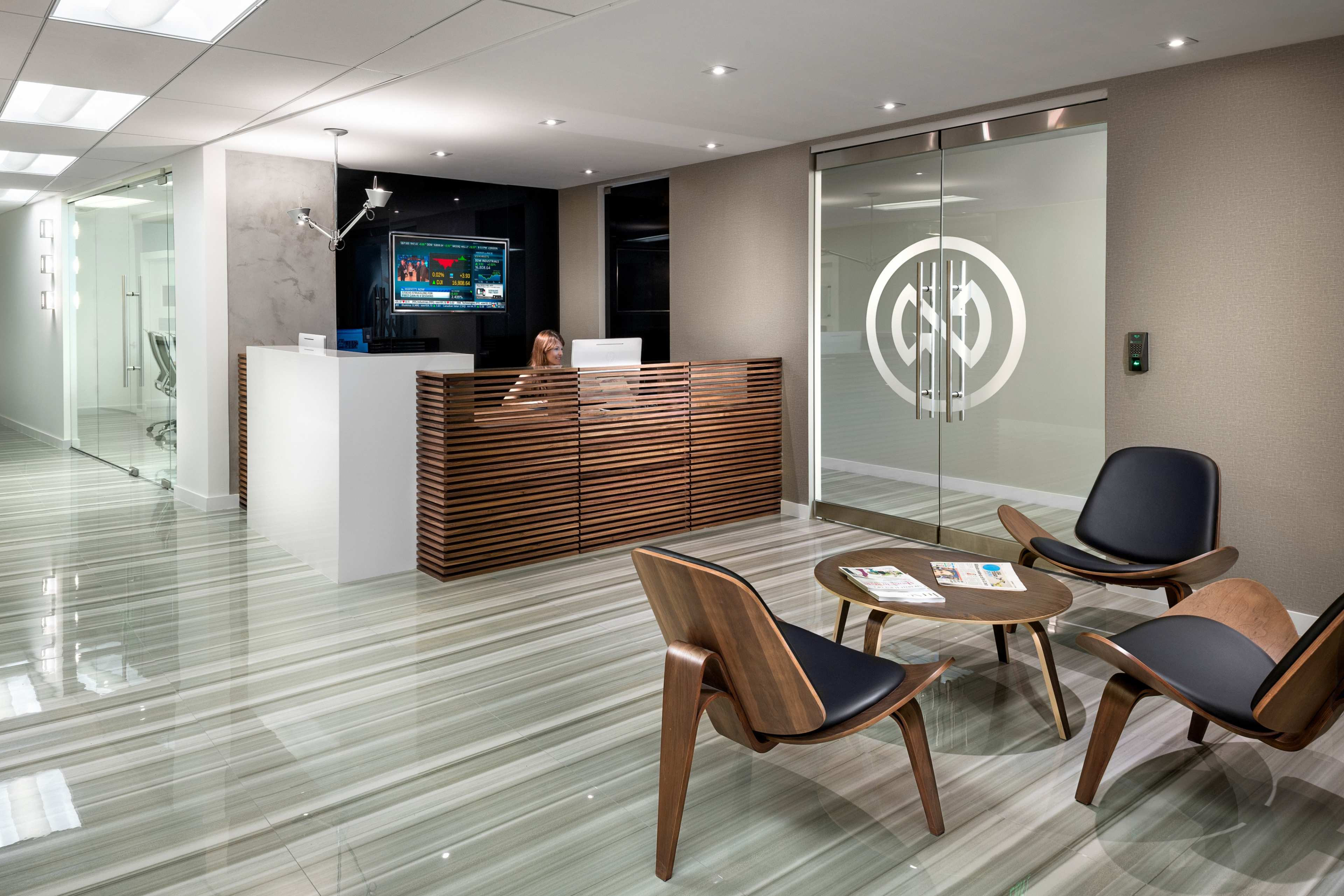 The image shows a modern office lobby with a reception desk, seating area, and glass doors featuring a logo.