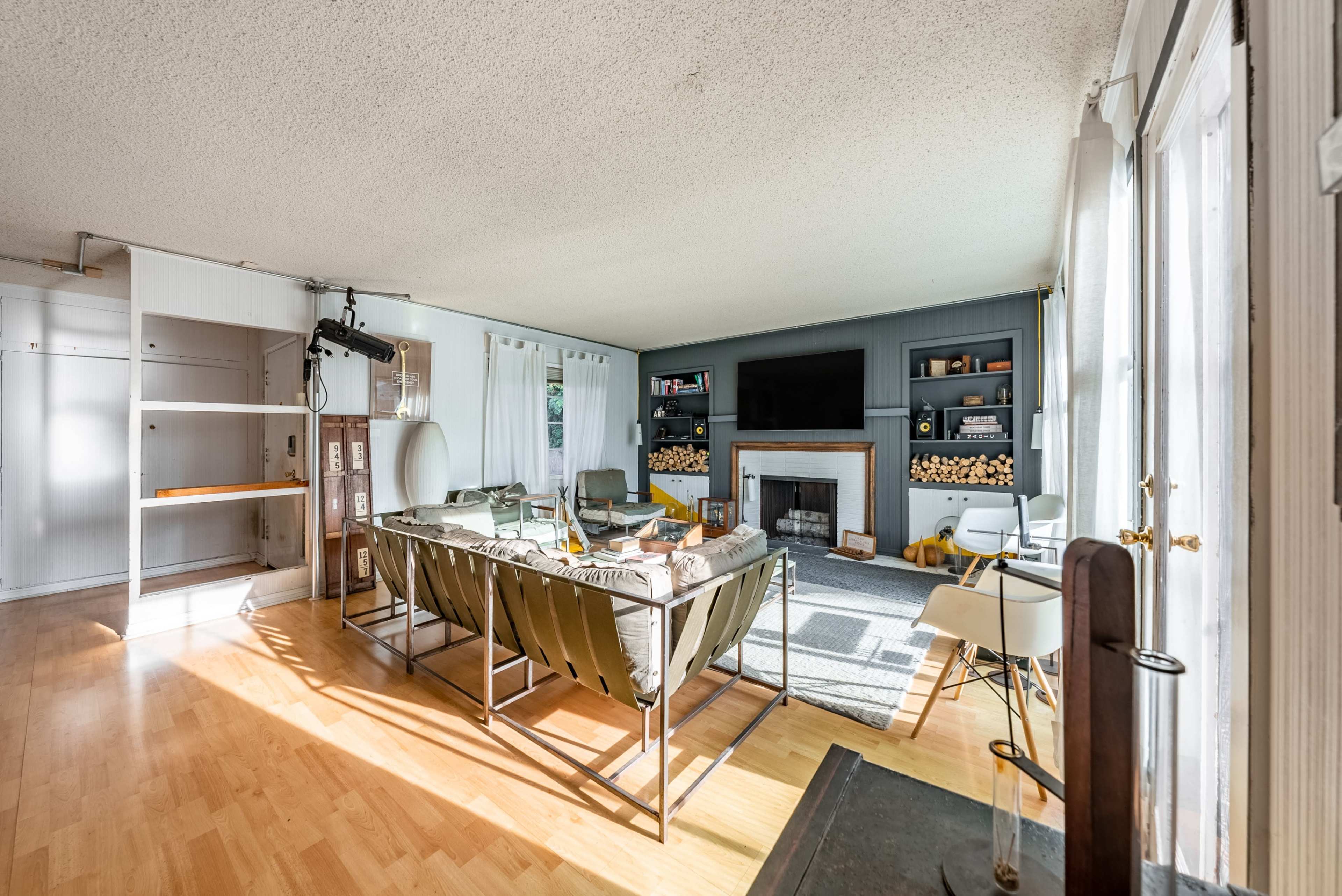 The living room features a fireplace, gray walls, and a seating area with minimalist furniture, including a mix of chairs and a sofa.