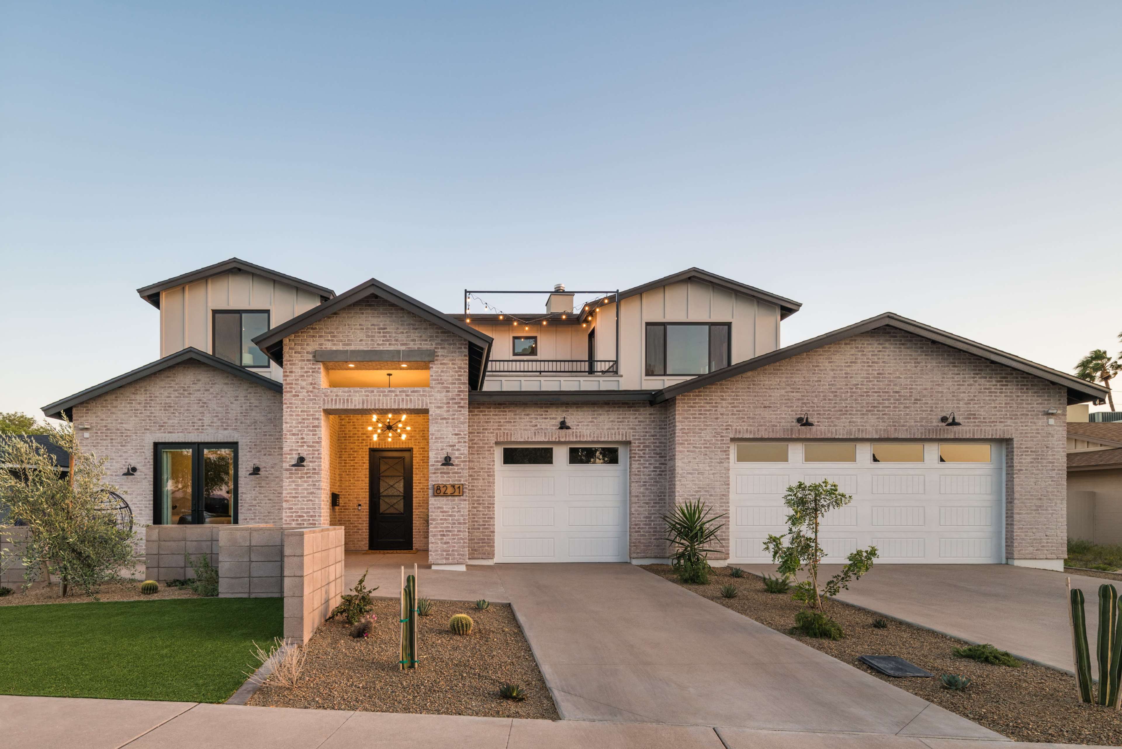 A modern two-story brick house with a landscaped front yard and two garage doors.