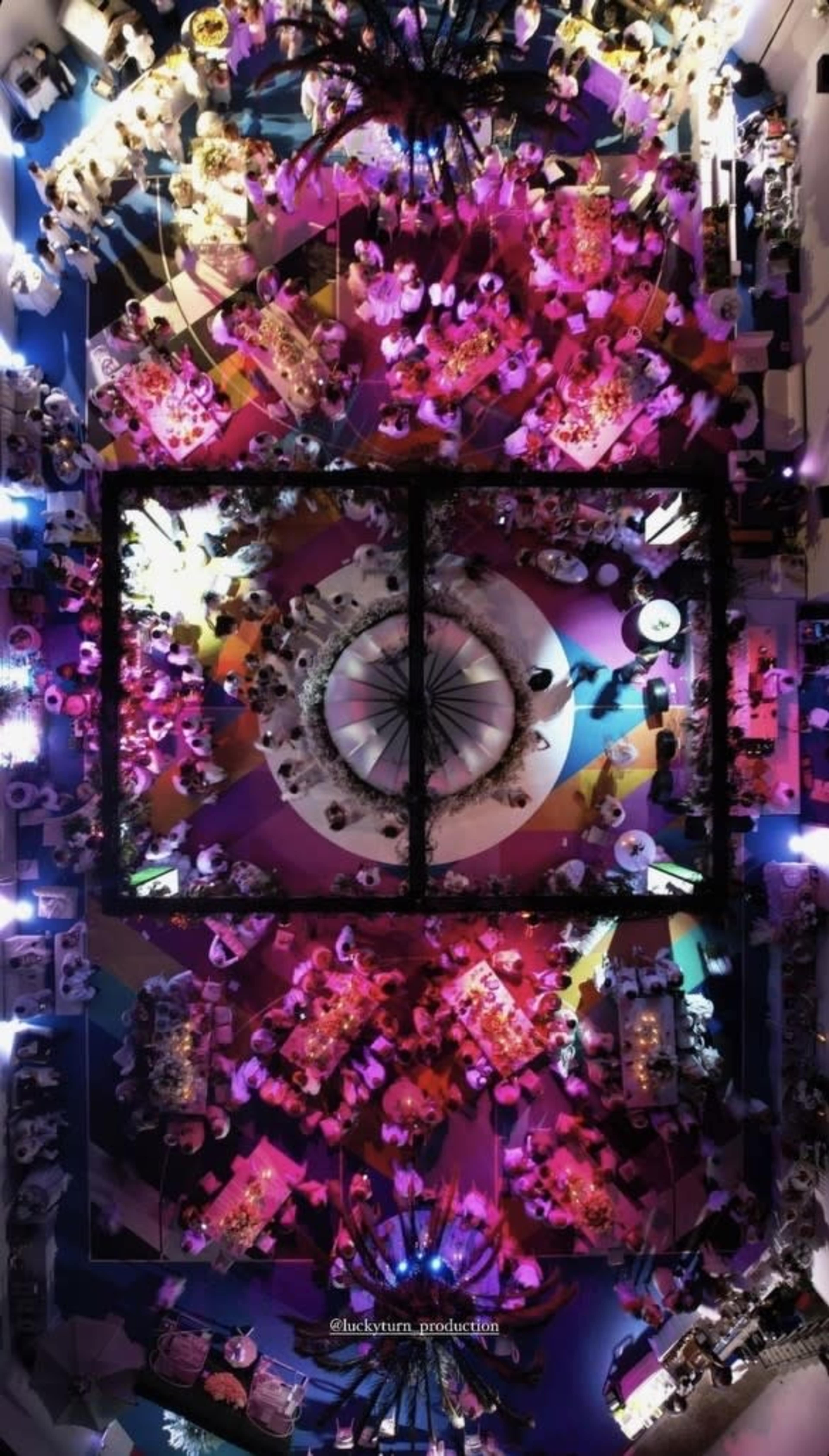 An overhead view of a banquet hall filled with tables, colorful lighting, and attendees enjoying a formal gathering.