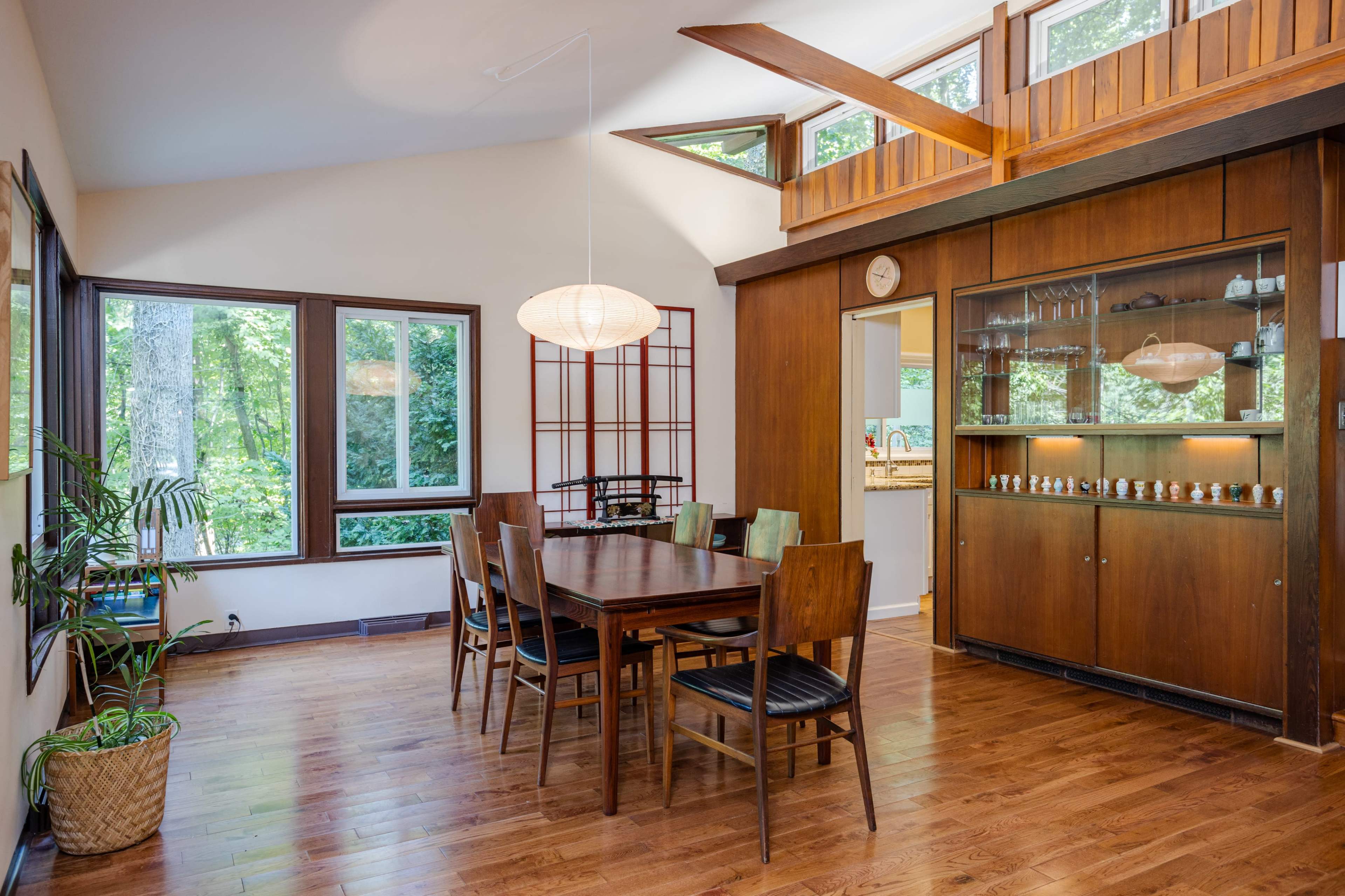 A dining room featuring a wooden table surrounded by chairs, large windows, and a built-in cabinet displaying various items.