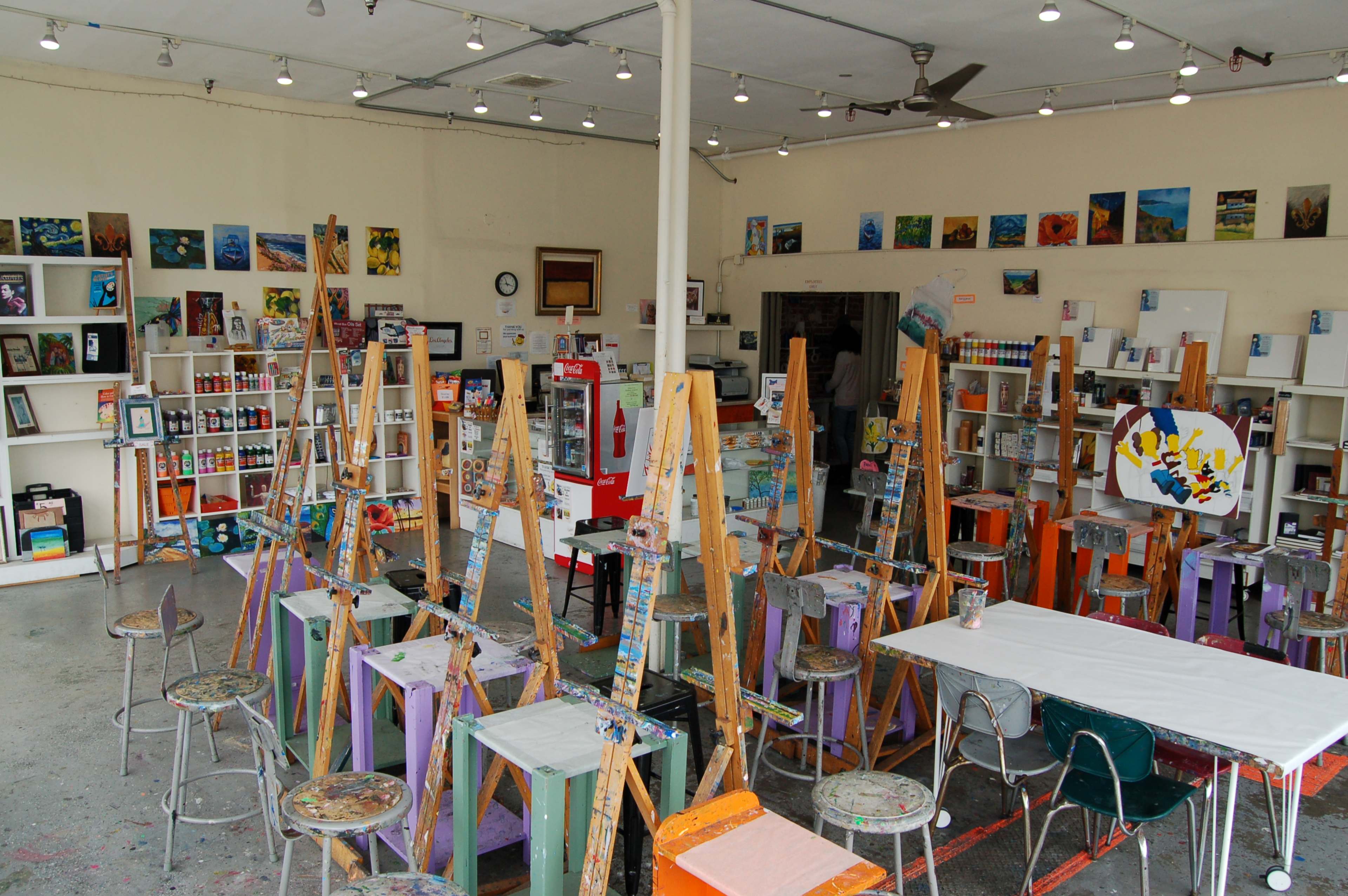 An artist studio filled with easels, stools, and shelves stocked with art supplies and paintings on the walls.