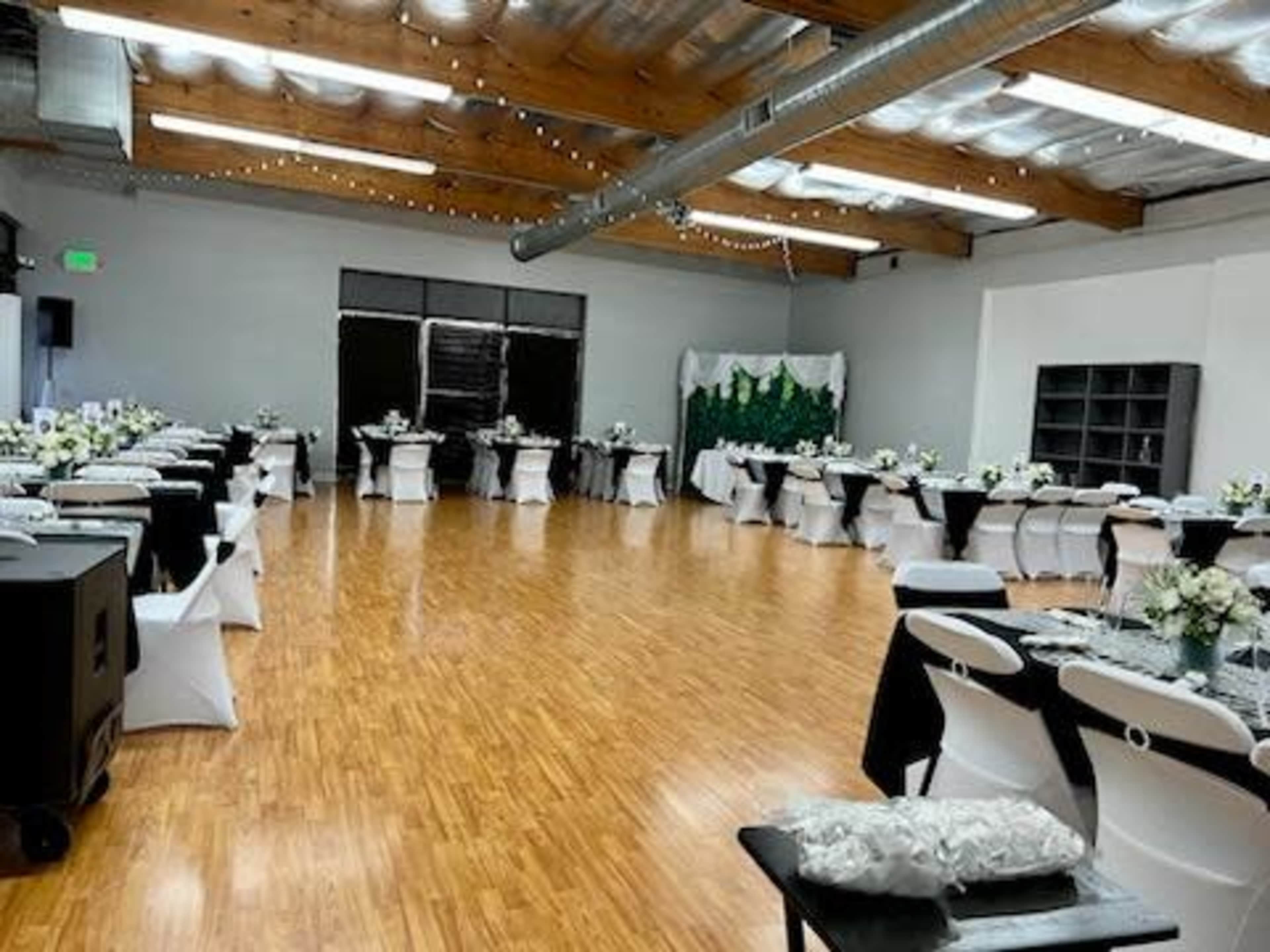 A spacious event hall is set up for a formal gathering, featuring tables covered with black and white linens adorned with floral centerpieces.