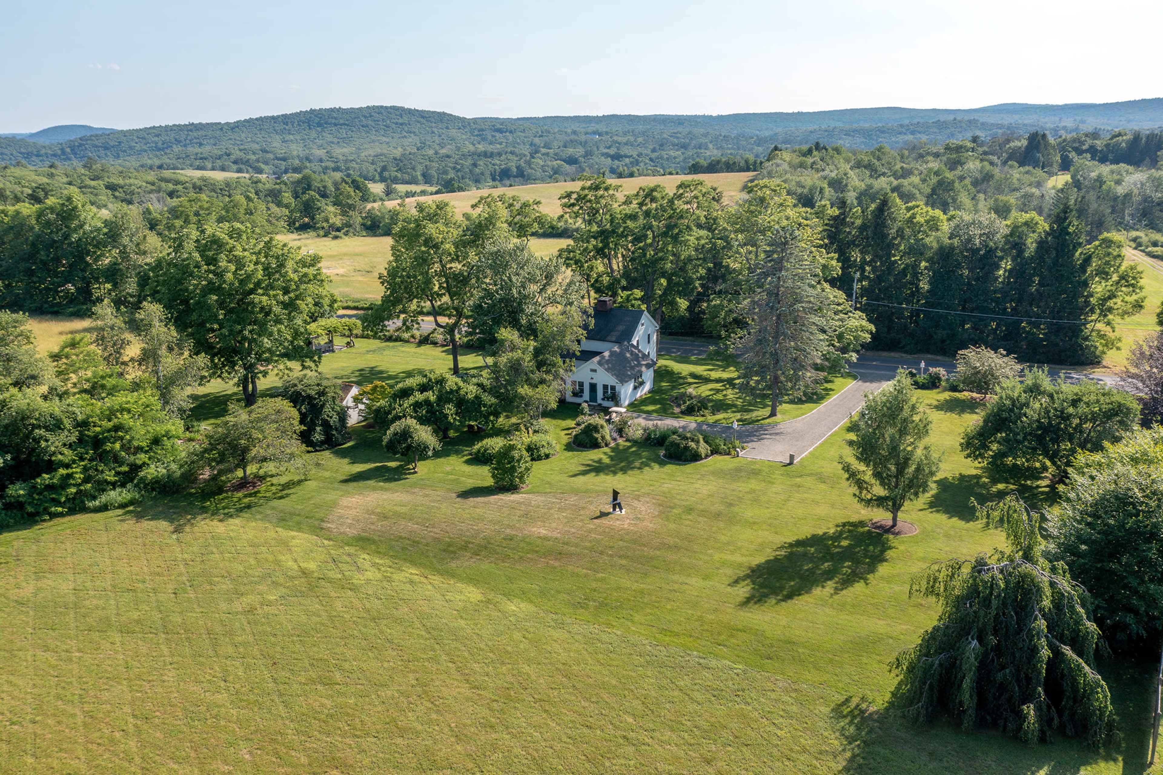 Aerial view of a house surrounded by landscaped grounds and trees, with rolling hills in the background.