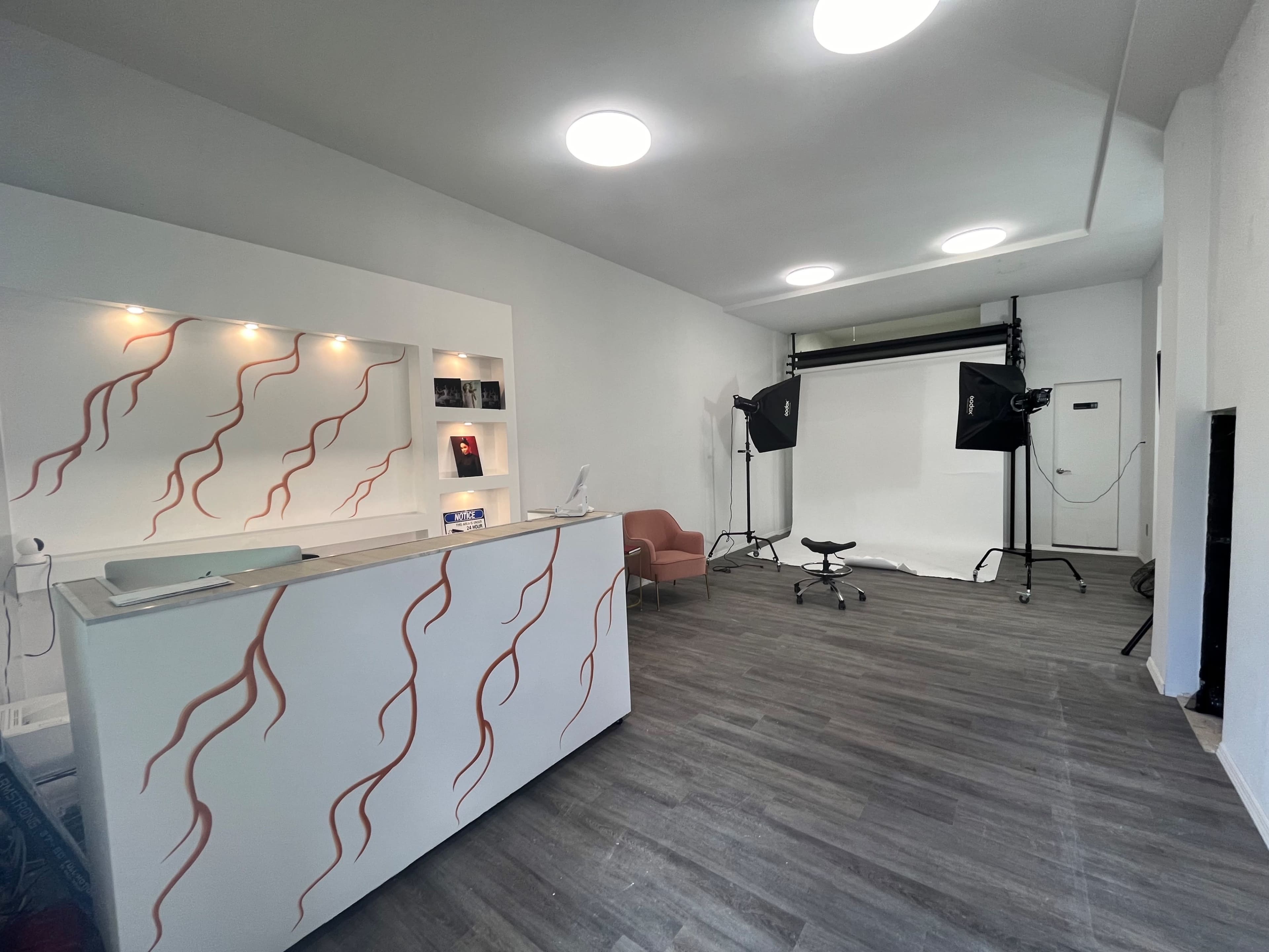A modern, well-lit interior space with a reception area featuring a white counter and a photography setup at the back with studio lighting.