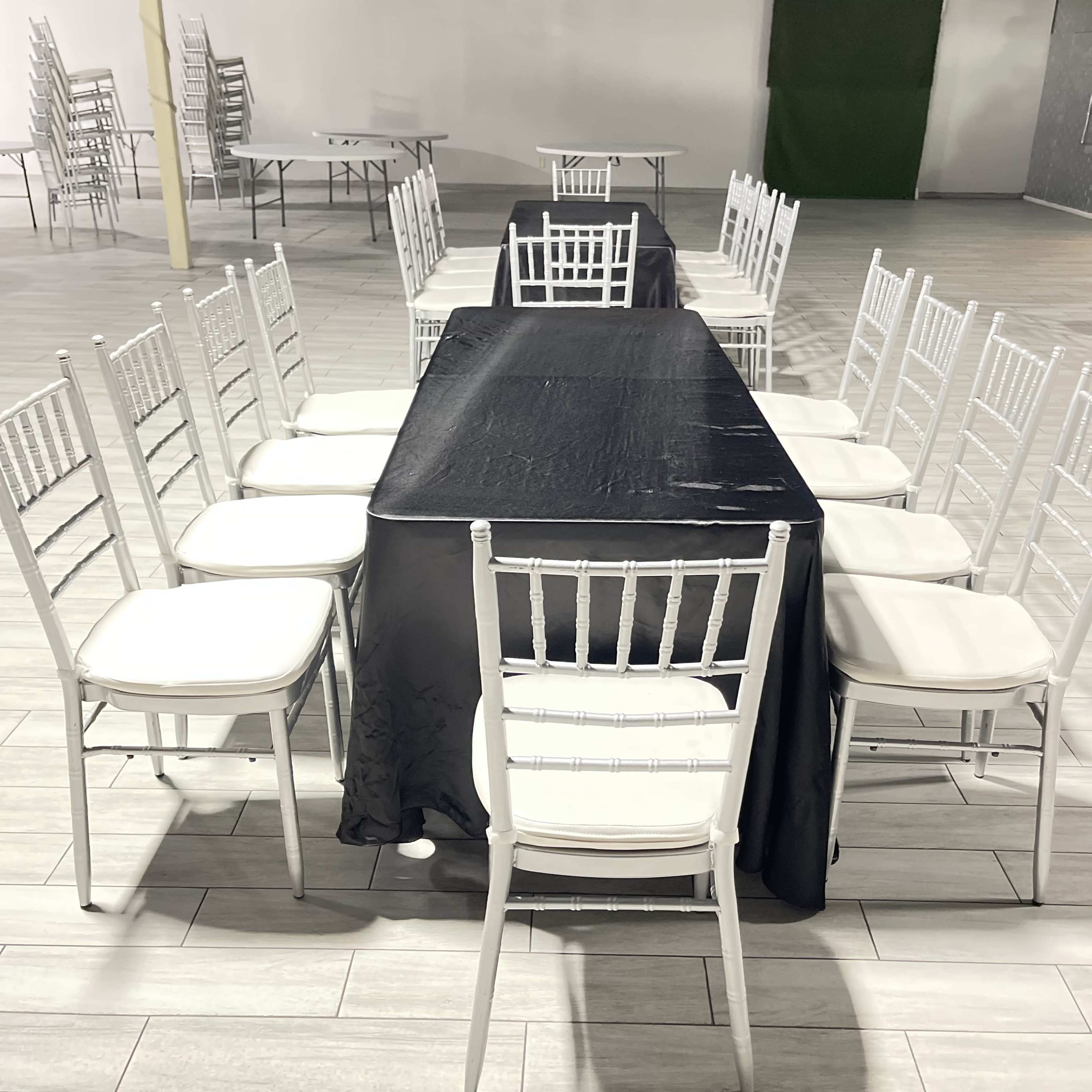 A long black table is set up with white chairs arranged around it in an empty room.