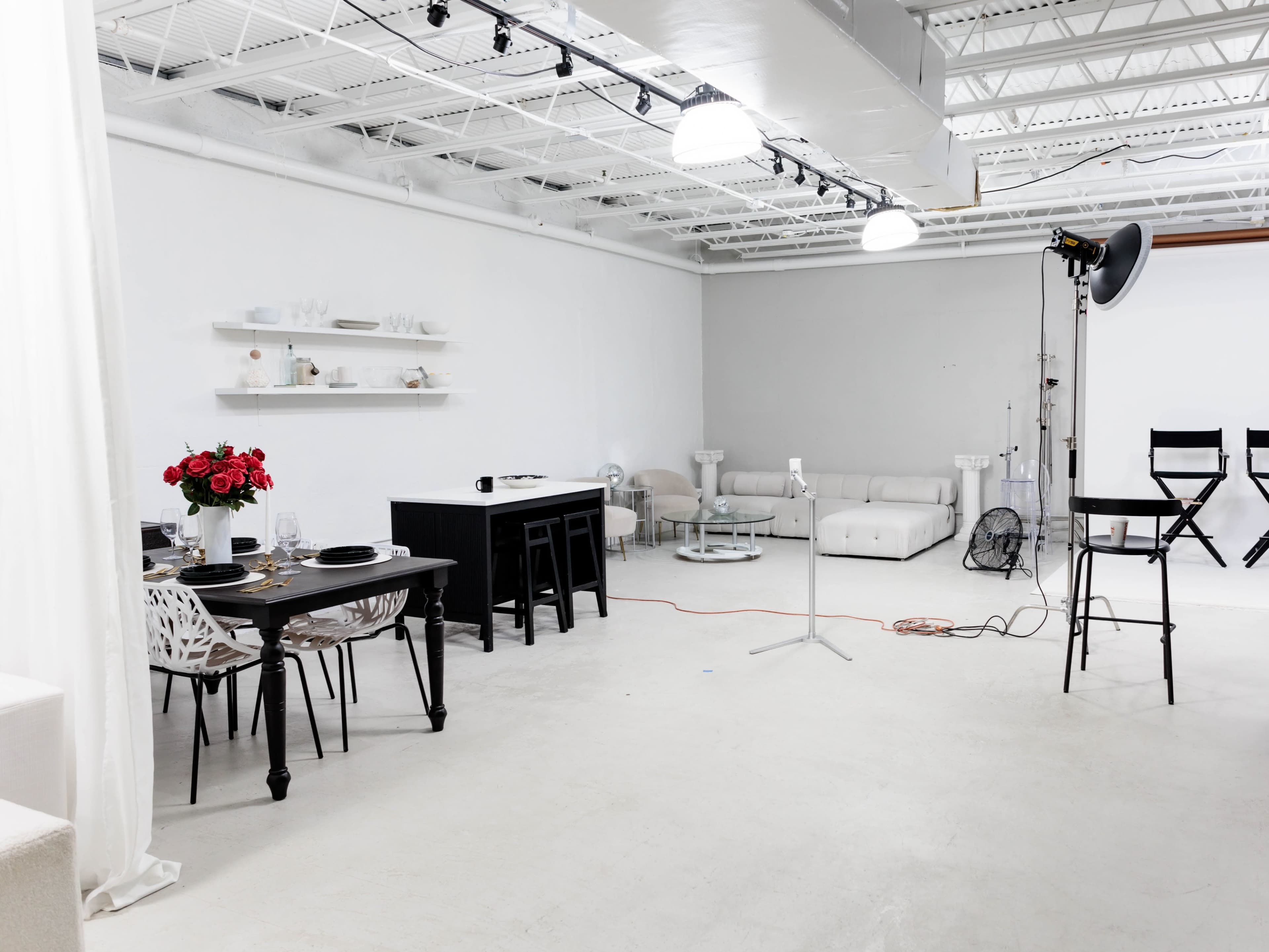 A spacious, minimalist studio with a dining table set for a meal, a couch area, and photography equipment positioned in one corner.