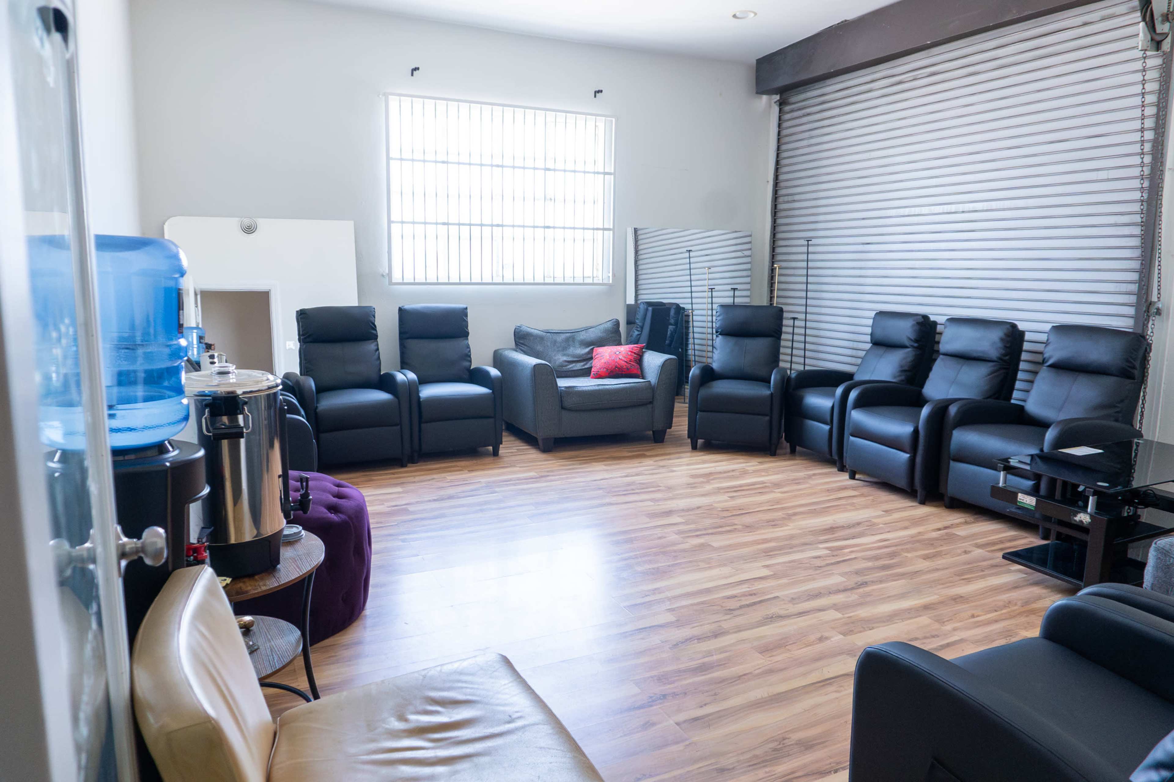 The image shows a spacious room arranged with several seating options, including black recliners and a water cooler, creating a meeting or relaxation space.