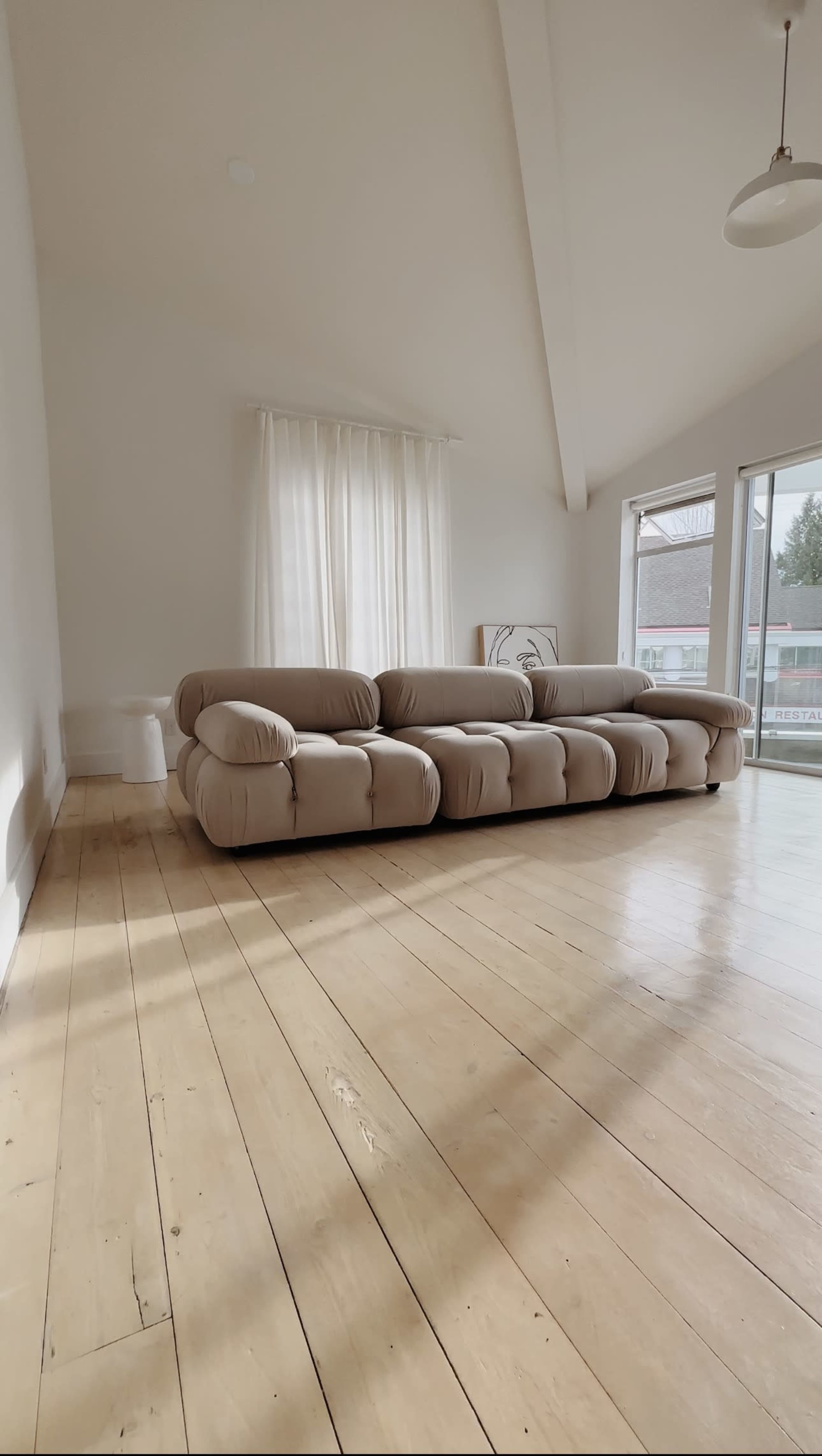 A spacious living room featuring a large, light-colored sofa and a large window with sheer curtains.