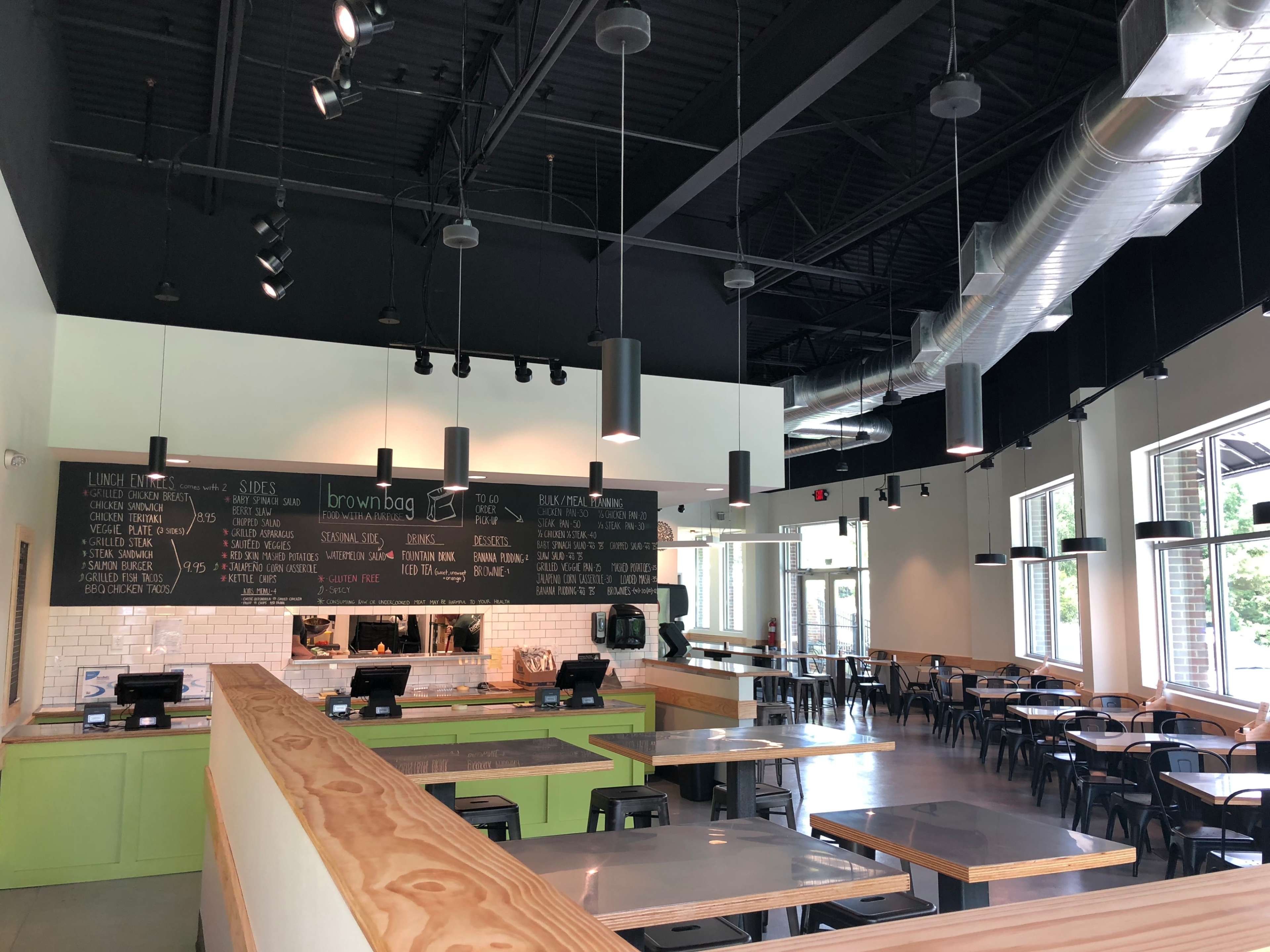 A modern restaurant interior with a service counter, multiple tables, and menu items displayed on a chalkboard.