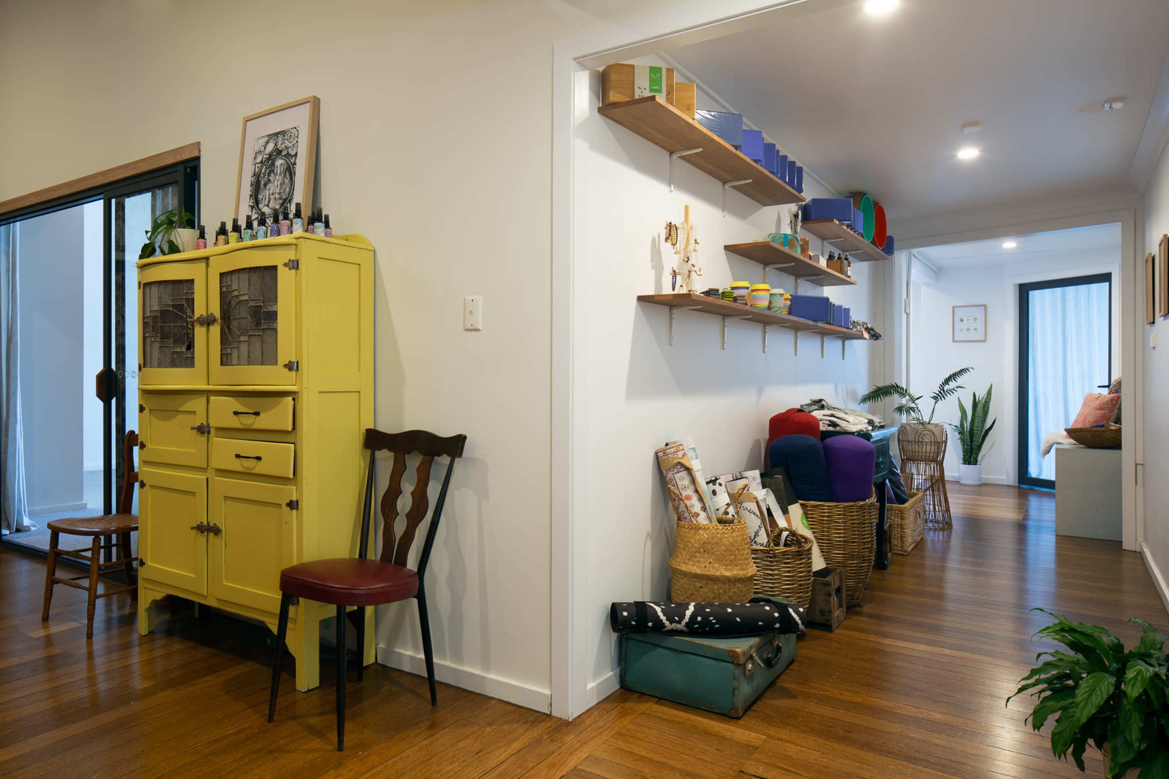 A well-lit hallway featuring a yellow cabinet, a chair, and shelves stocked with various items along the walls.