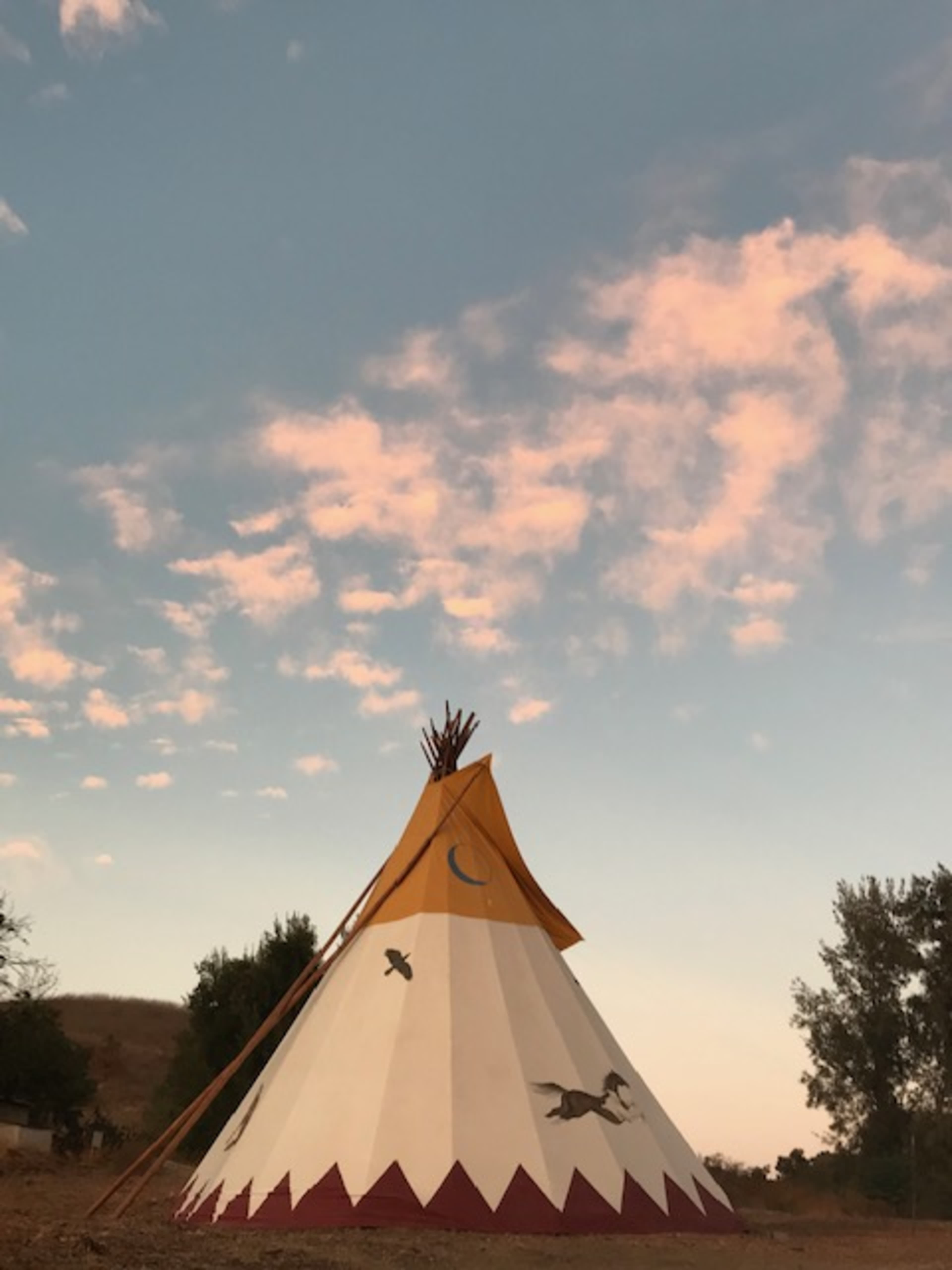 A tent-like structure with a conical shape and painted patterns stands against a sky with scattered clouds at dusk.