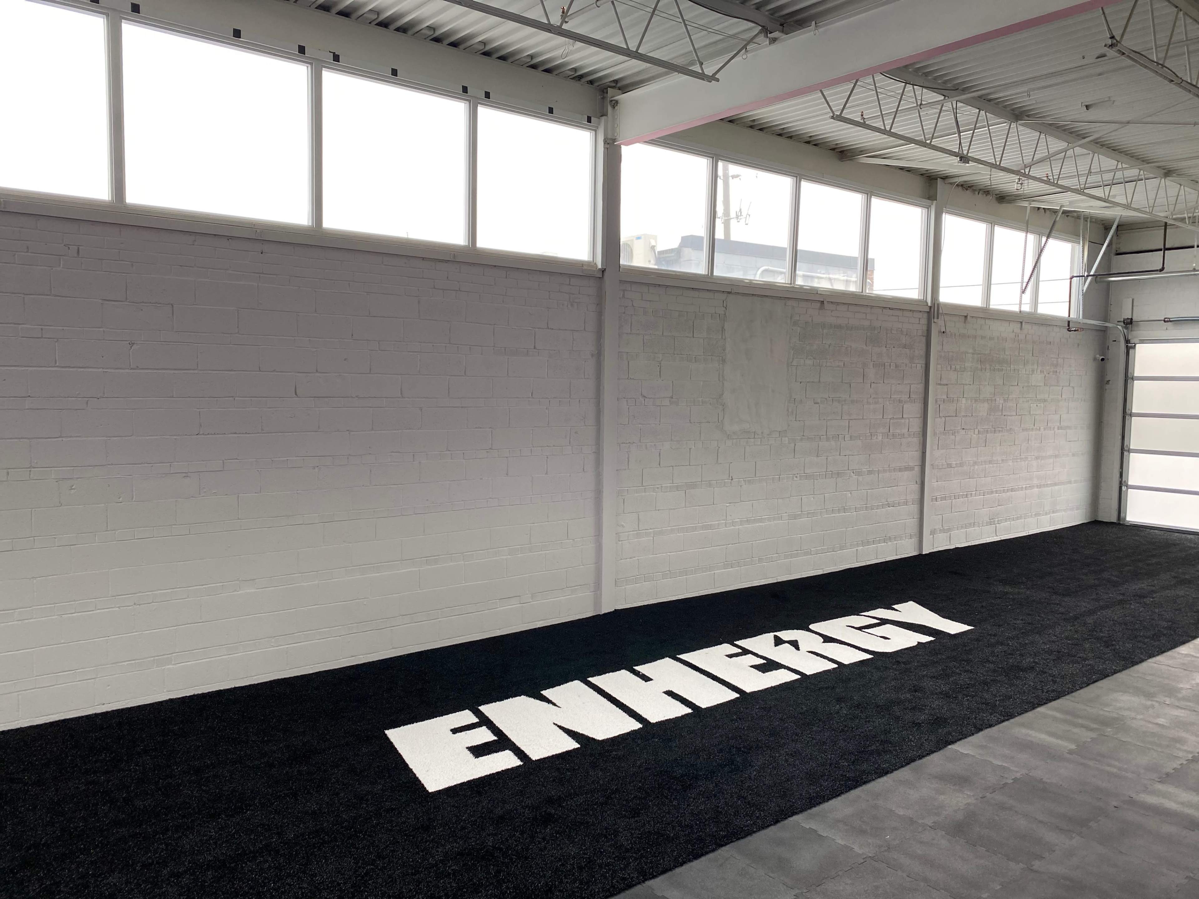 A spacious indoor area with a black carpet featuring the word "ENERGY" prominently displayed on the floor, against a backdrop of white walls and large windows.