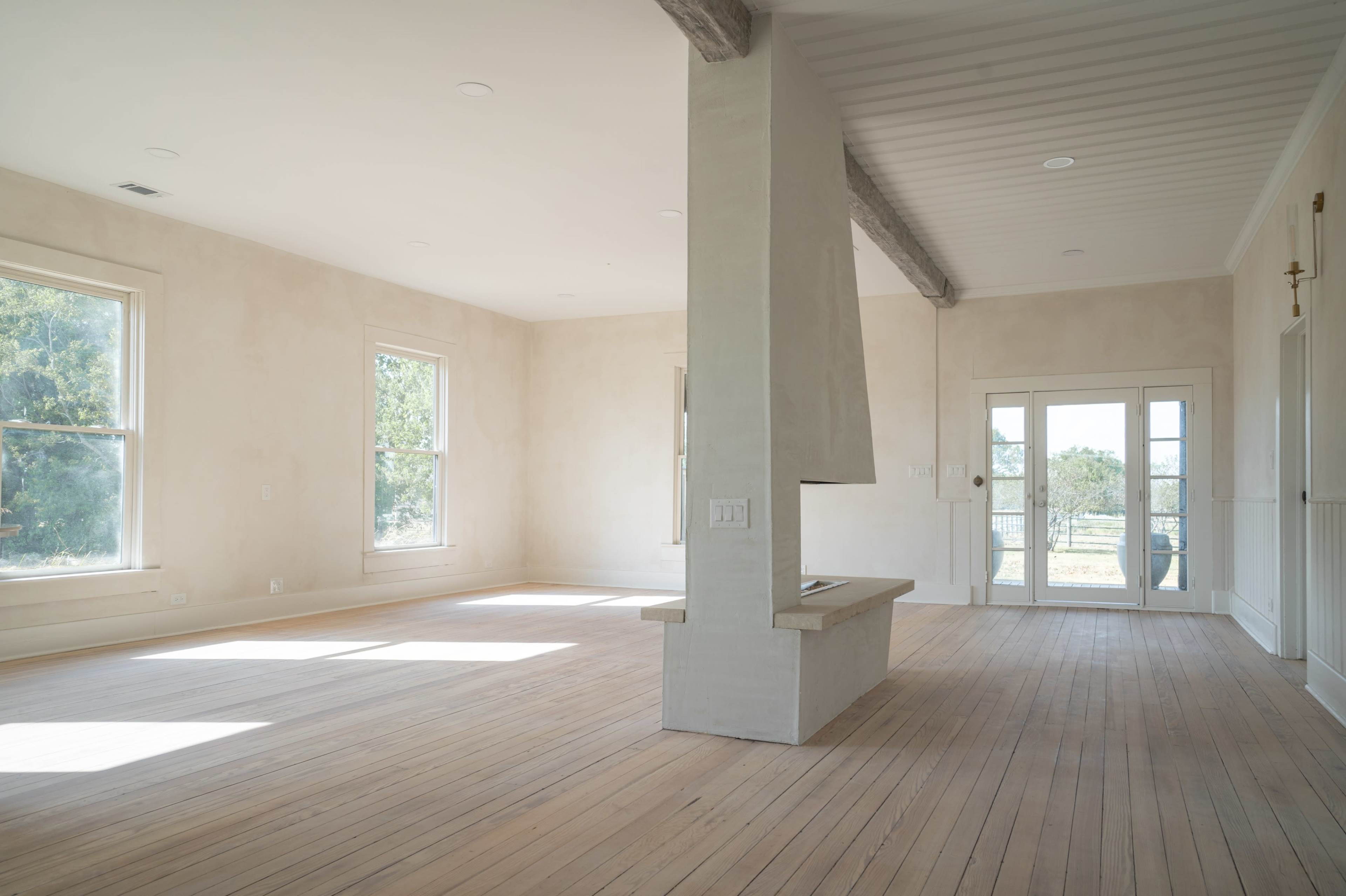 A spacious, empty room featuring light-colored walls, large windows, and a central column with a built-in bench.