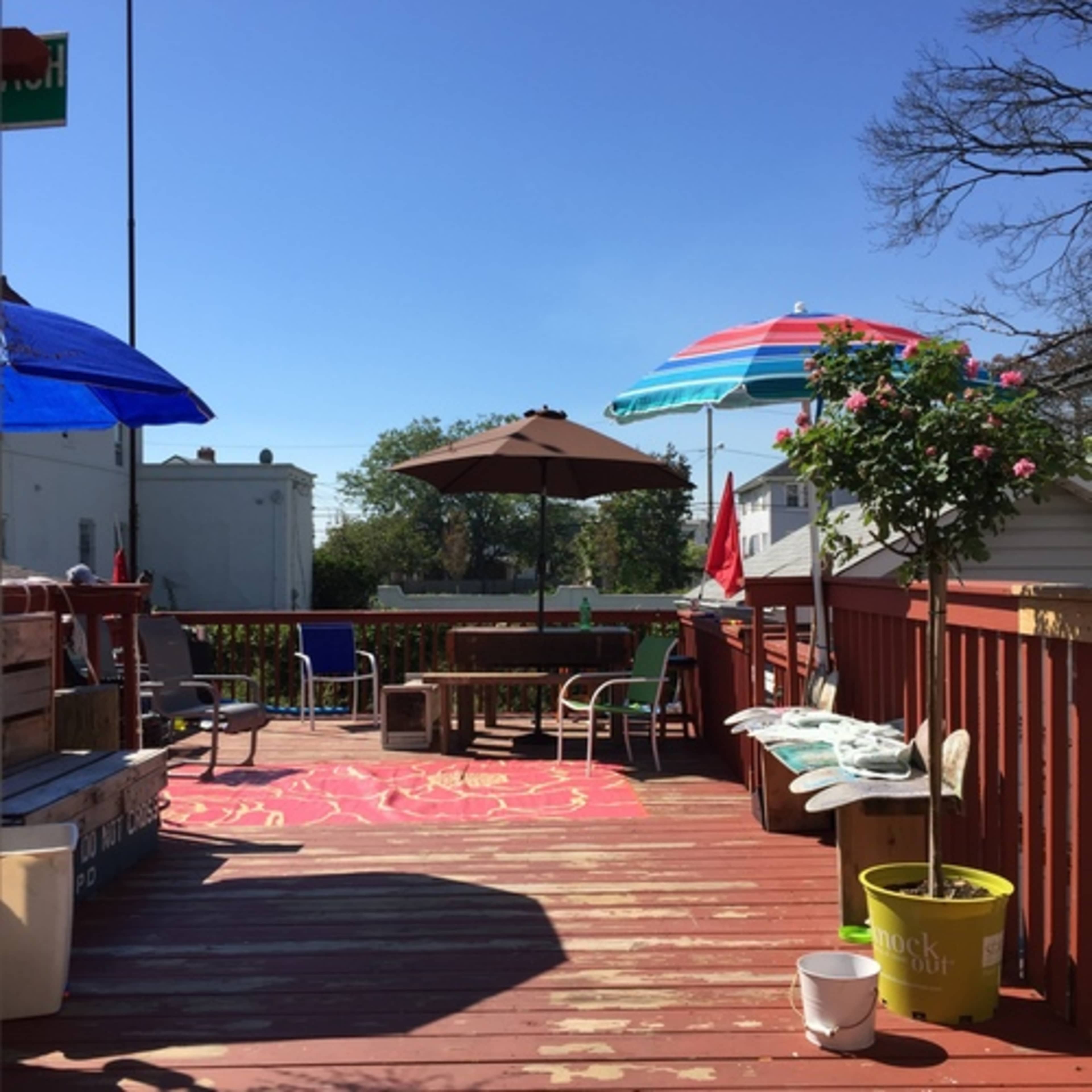 A wooden deck features colorful umbrellas, chairs, and potted plants under a clear blue sky.