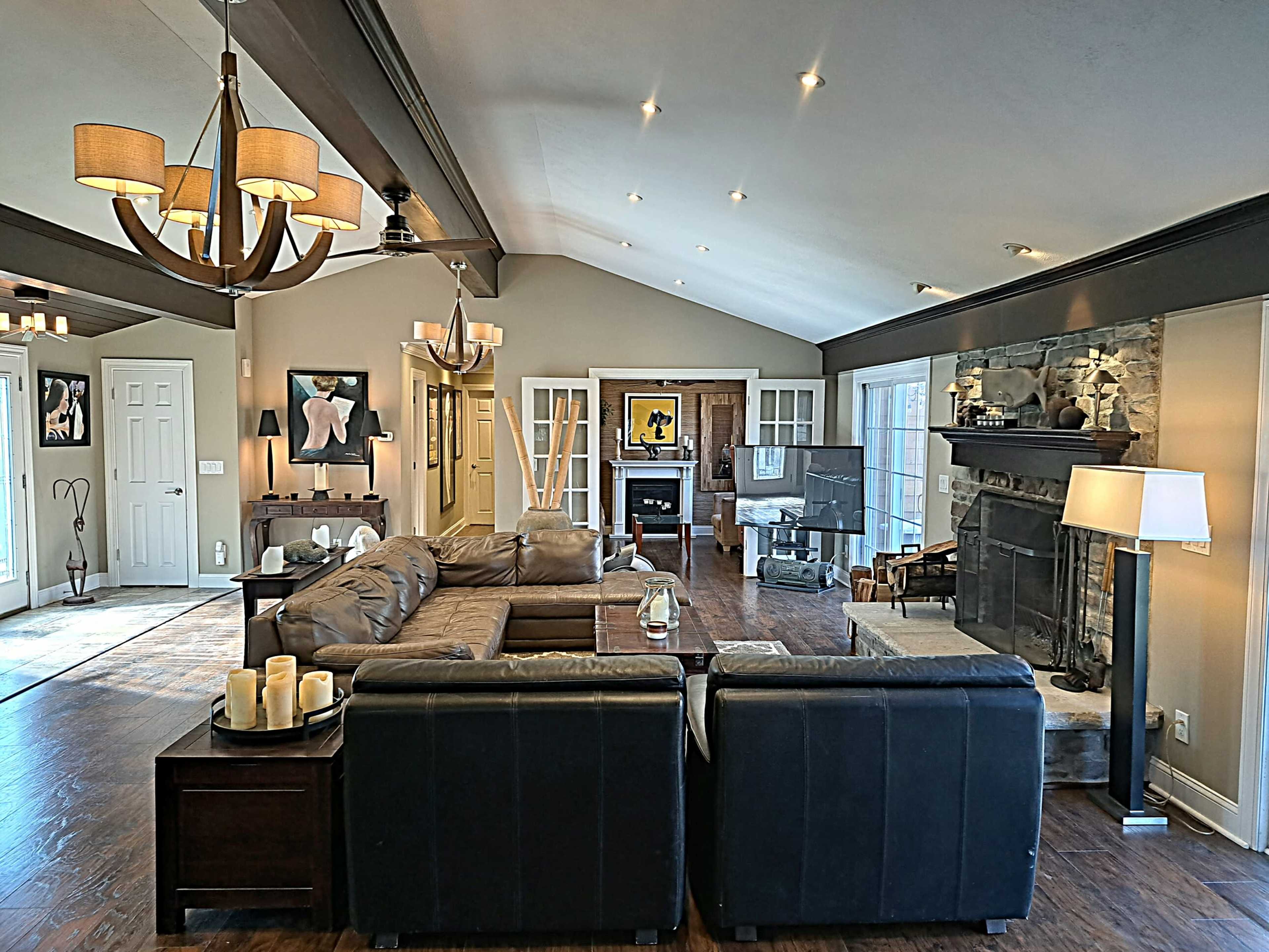 A spacious living room featuring a leather sofa set, a stone fireplace, and large windows that allow natural light to fill the space.