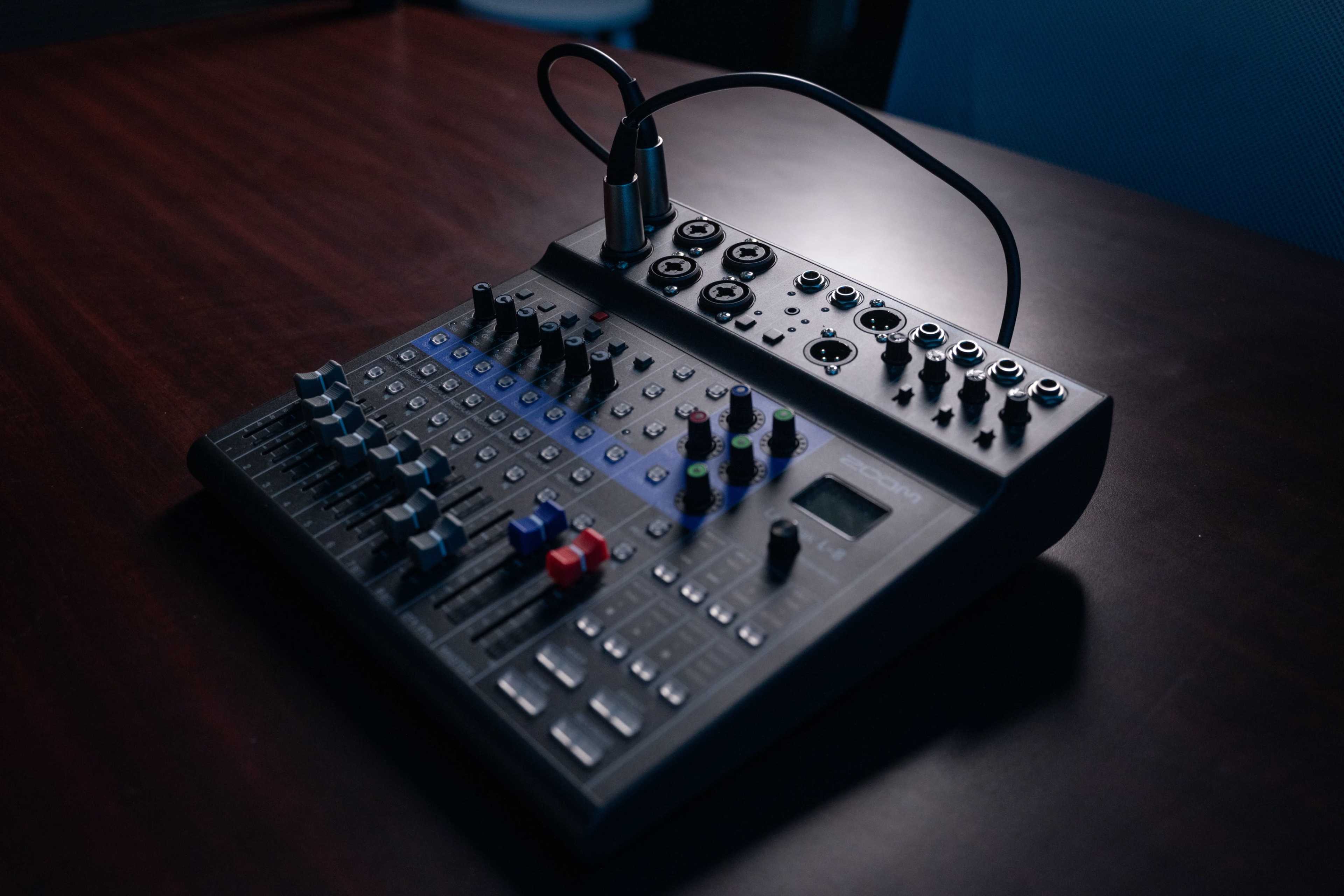 A black audio mixer with various knobs, switches, and input/output ports resting on a wooden surface.