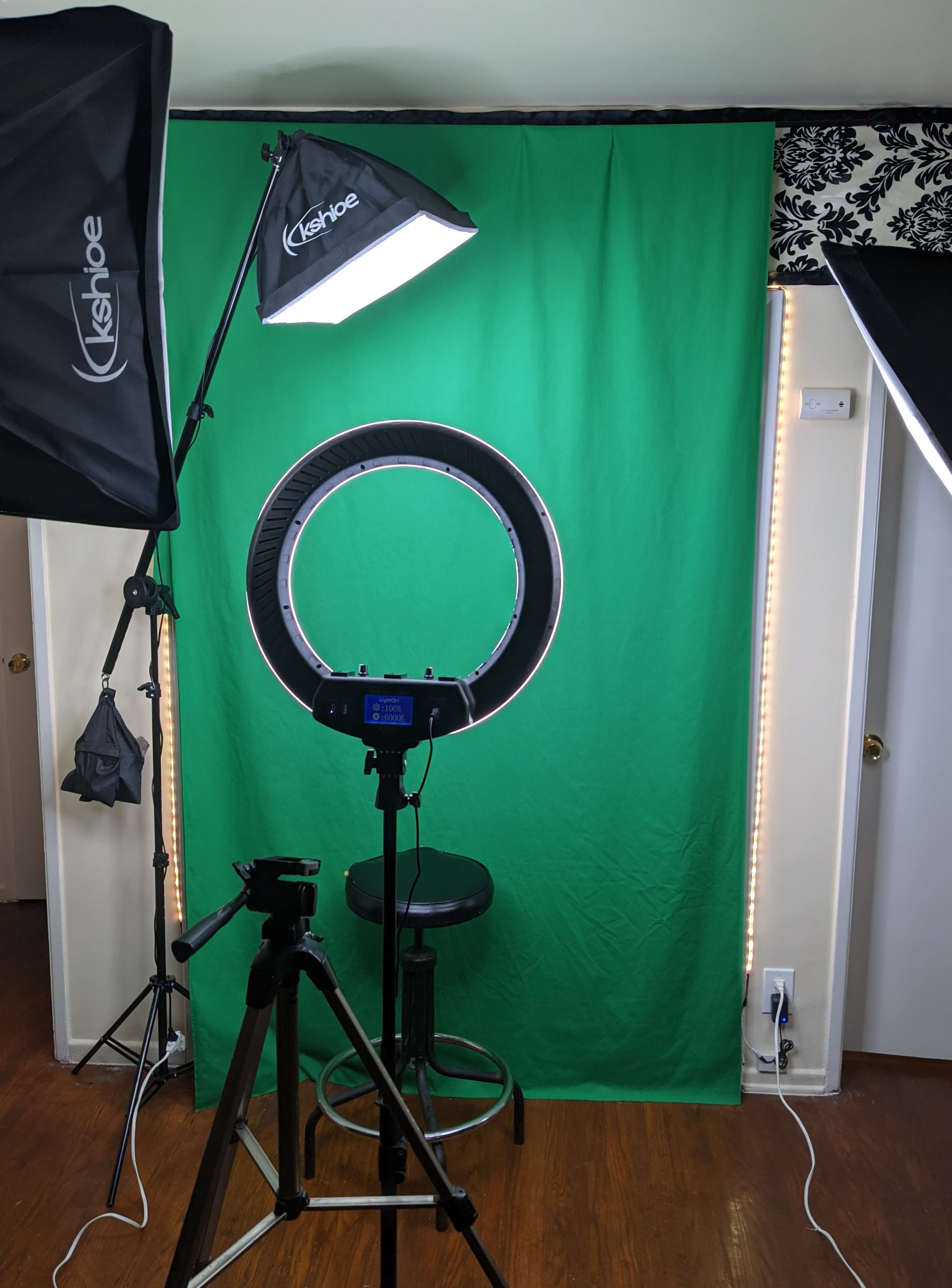 The image shows a photography setup with a green backdrop, a ring light, and a stool positioned in front of a camera on a tripod.