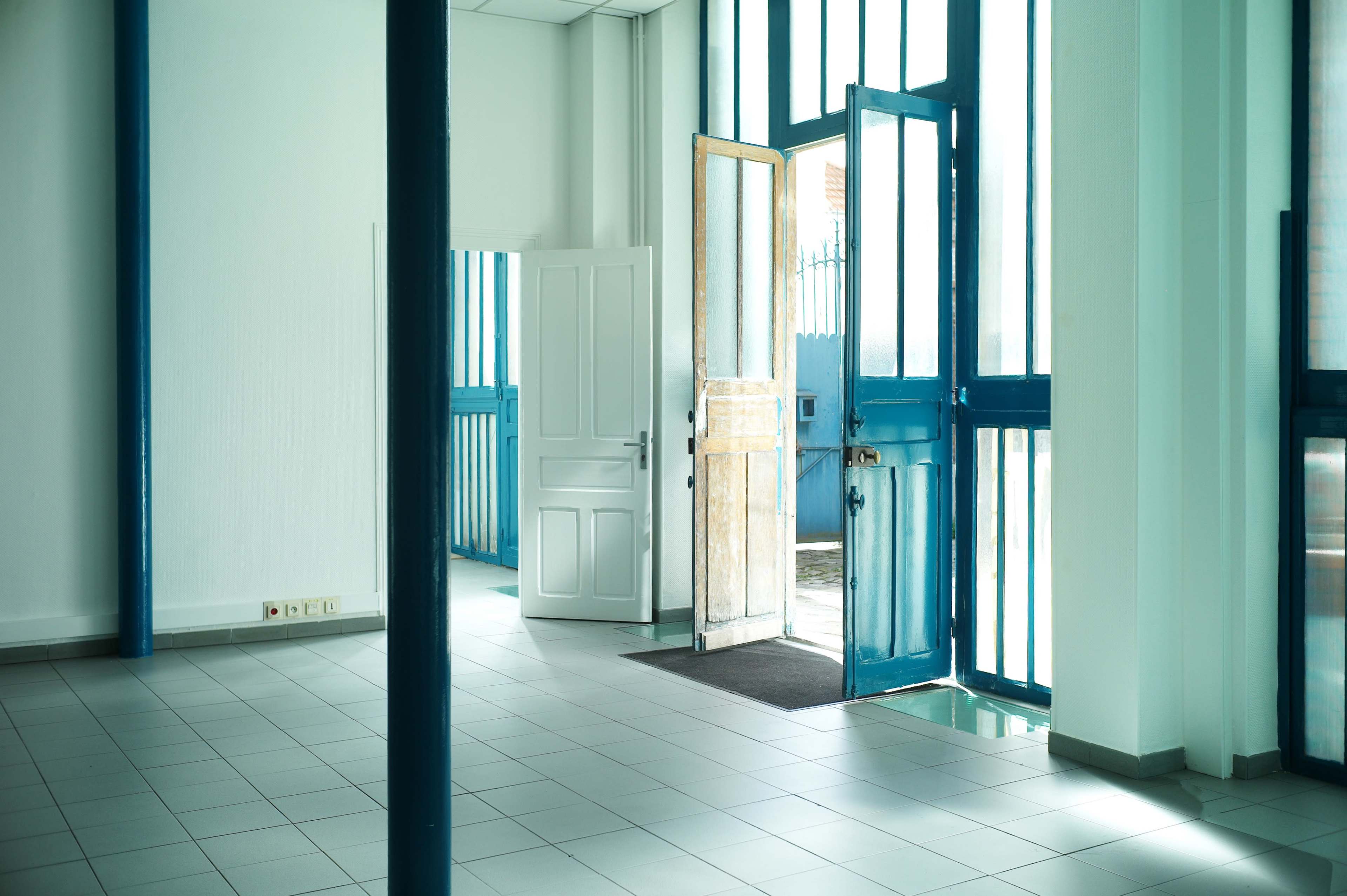 The image shows a bright, empty room with large windows and an open door, allowing light to stream in.
