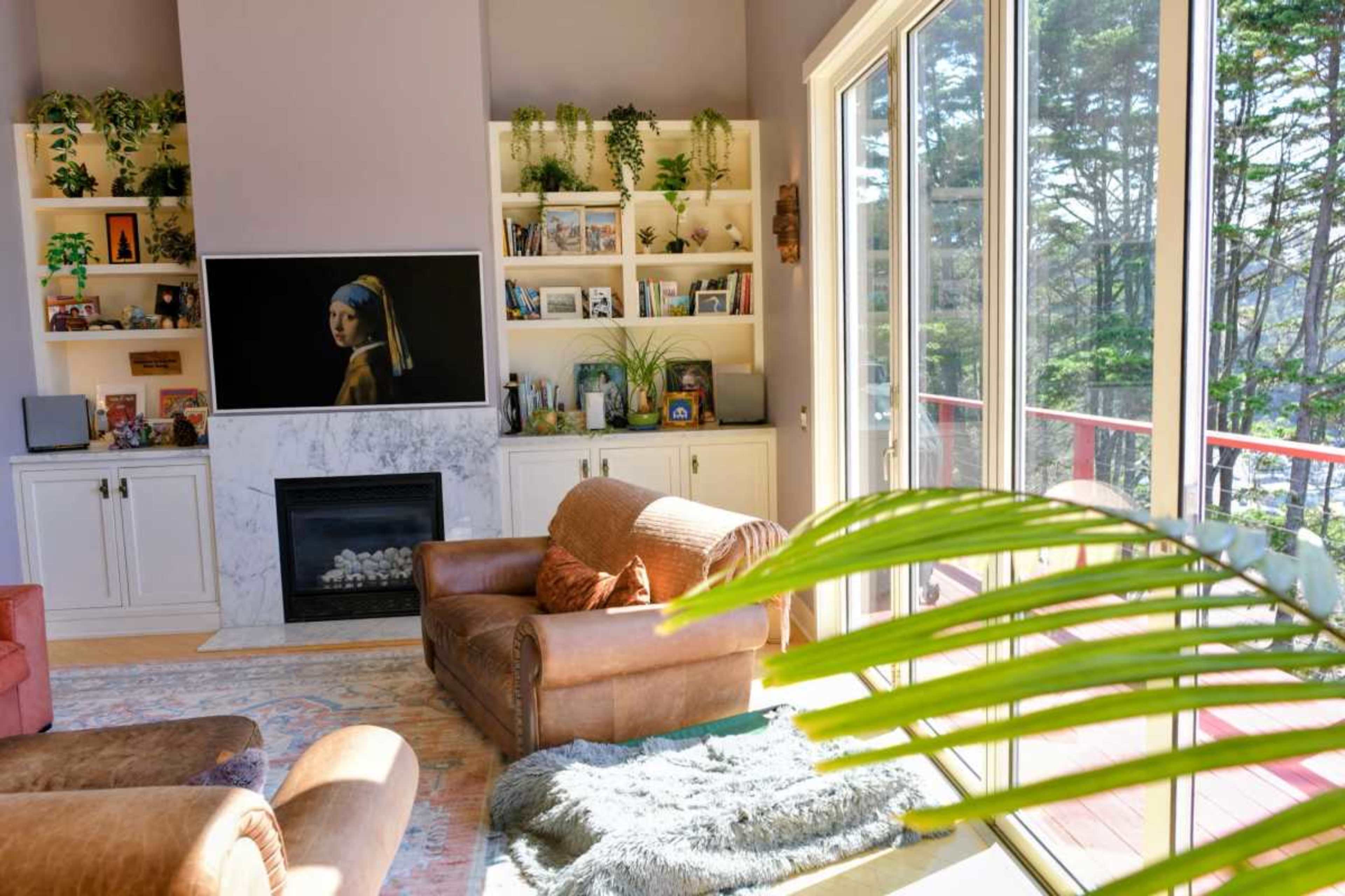 A modern living room features a large television mounted above a marble fireplace, surrounded by bookshelves filled with decorative items, and a cozy seating area with leather armchairs.