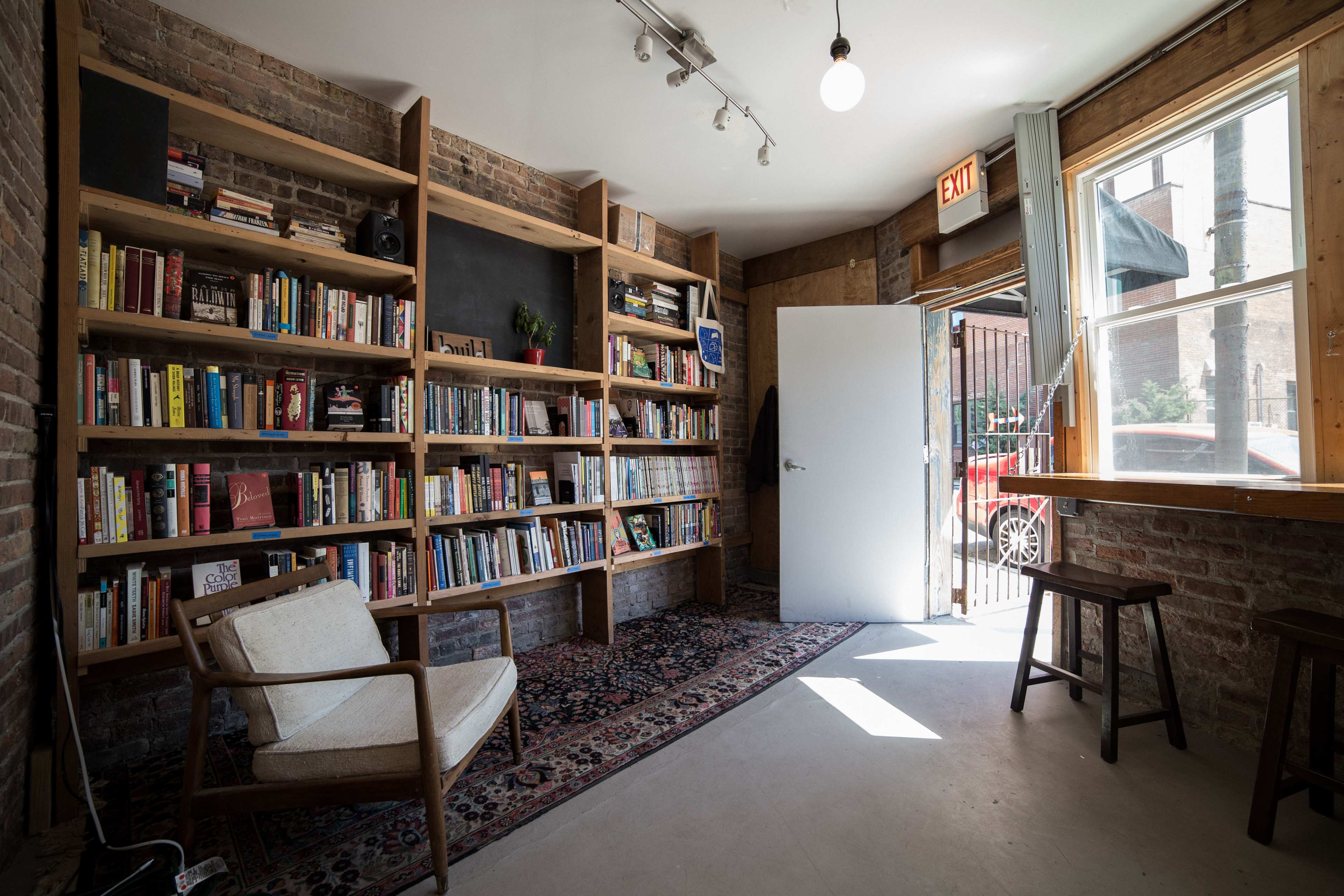 A cozy room with a bookshelf filled with books, a chair, and an open door leading outside.