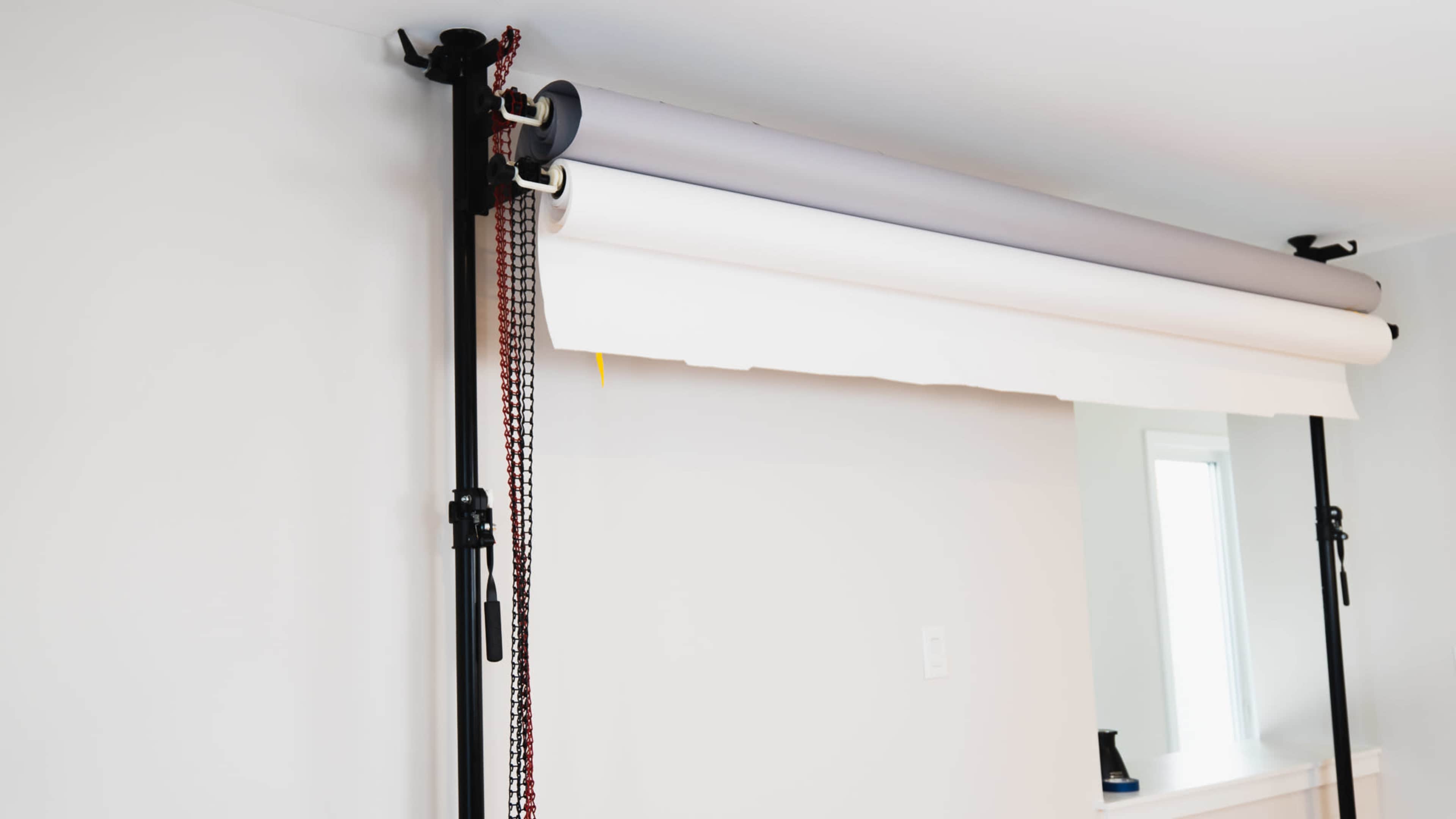 The image shows a backdrop support system mounted to a wall, featuring rolled paper backdrops in various colors.