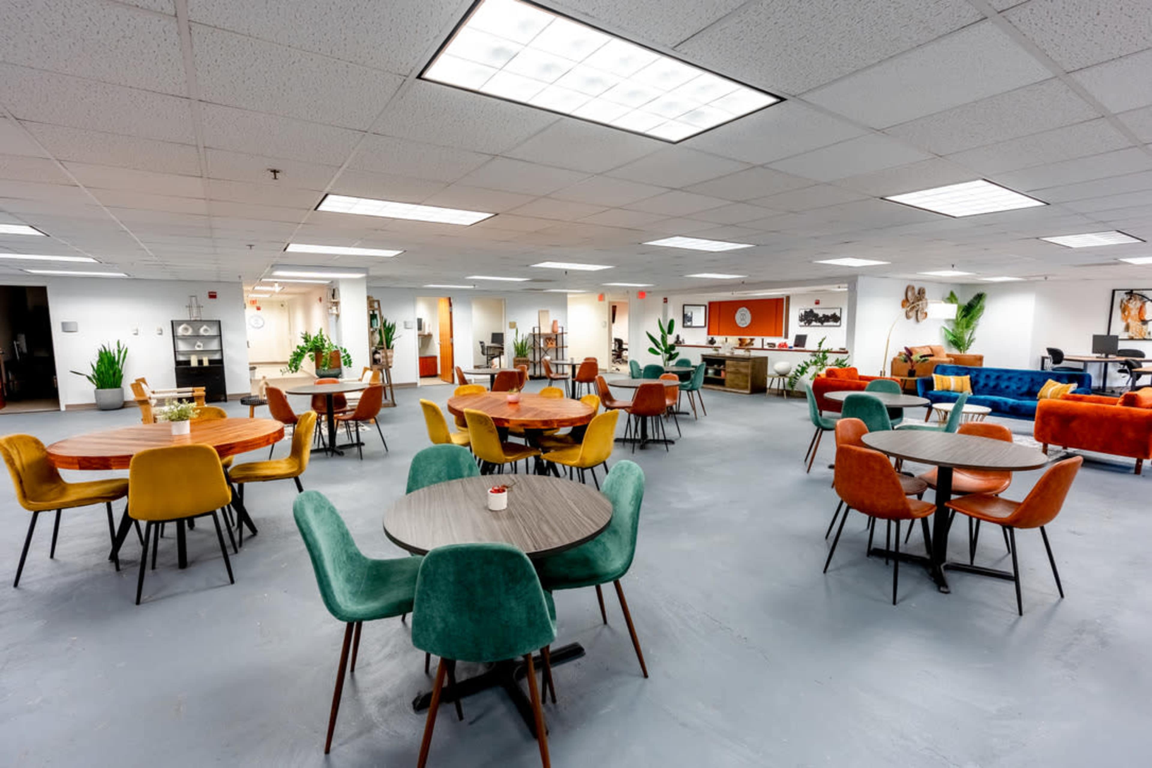 The image shows a spacious office area with multiple round tables and colorful chairs arranged throughout the space.