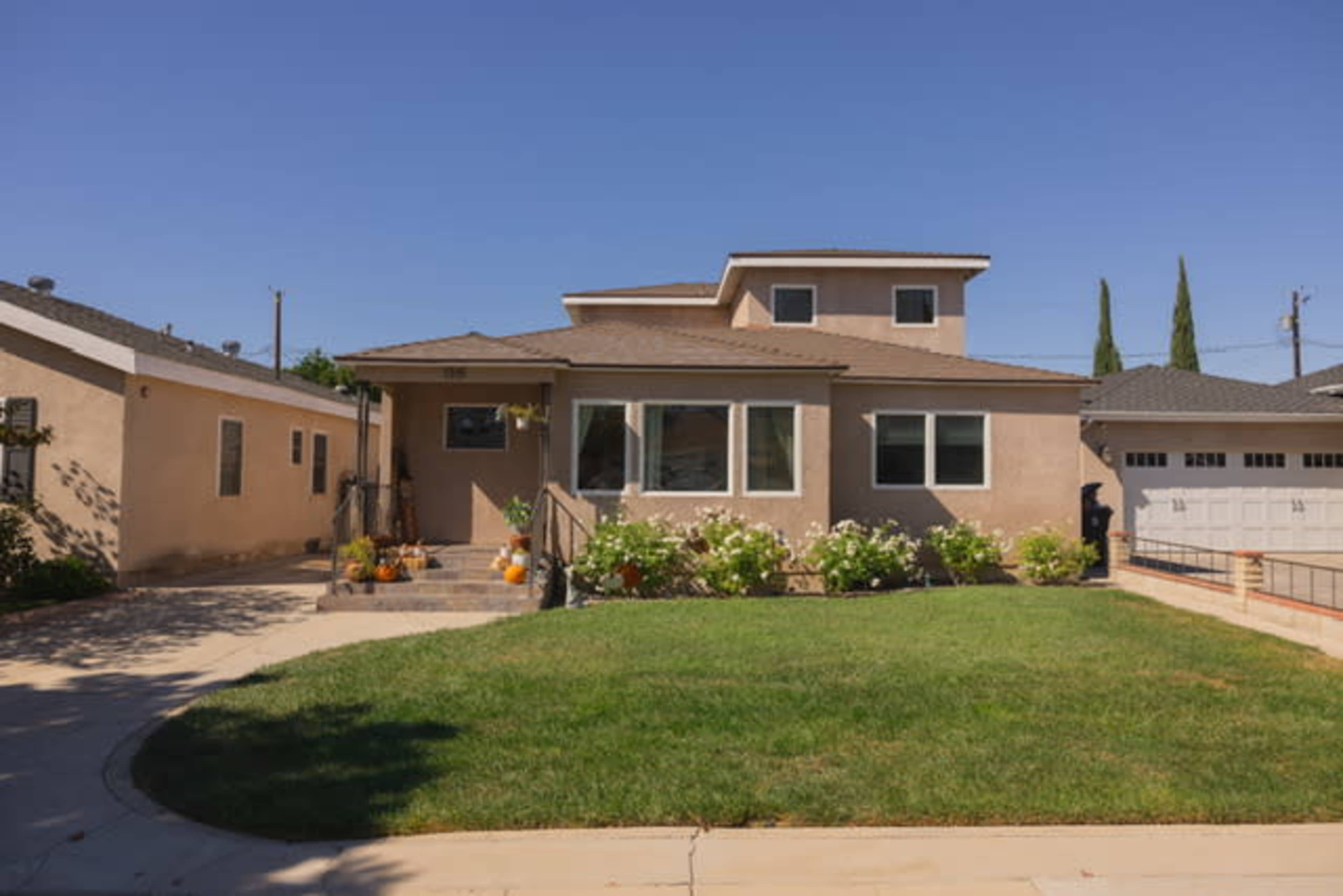 A two-story house with a landscaped front yard, featuring a mix of concrete driveway and light-colored exterior walls.