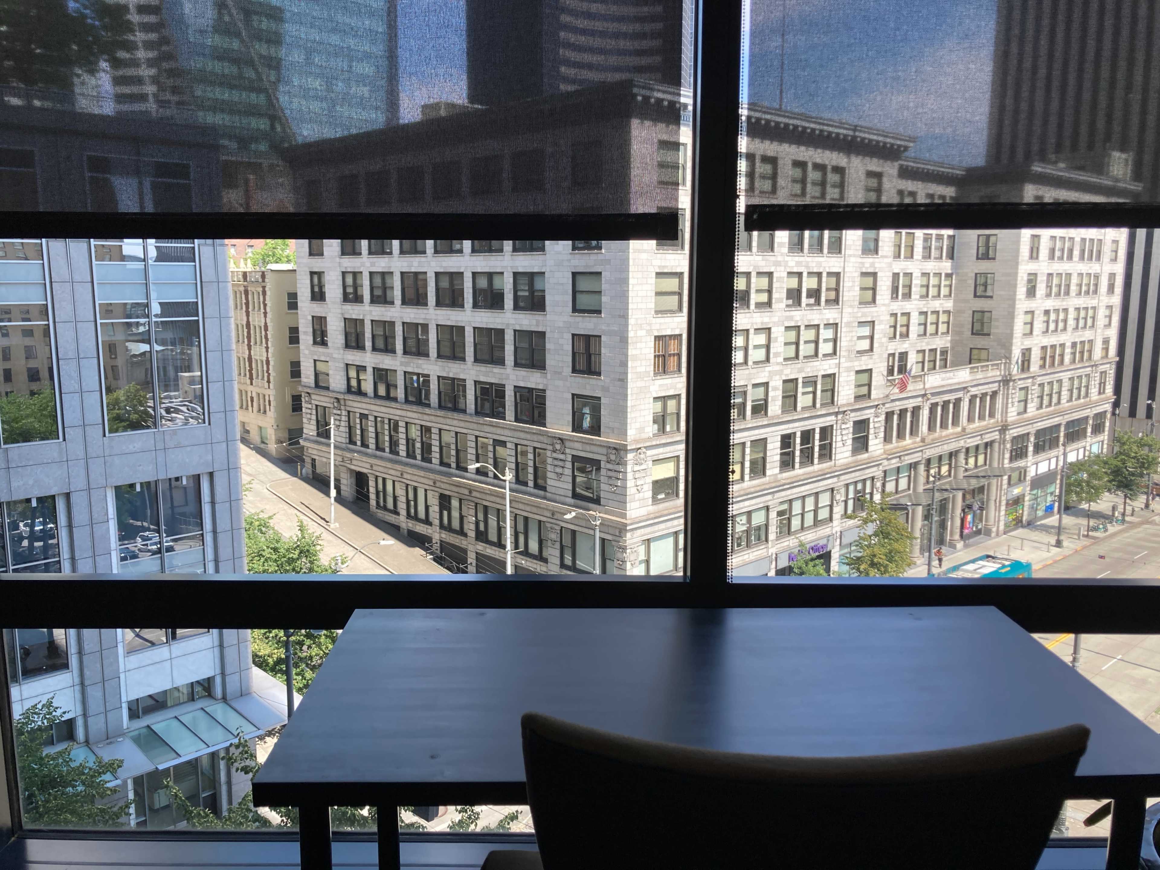 A view of a city street lined with historical buildings through a large window, with a table and chair in the foreground.