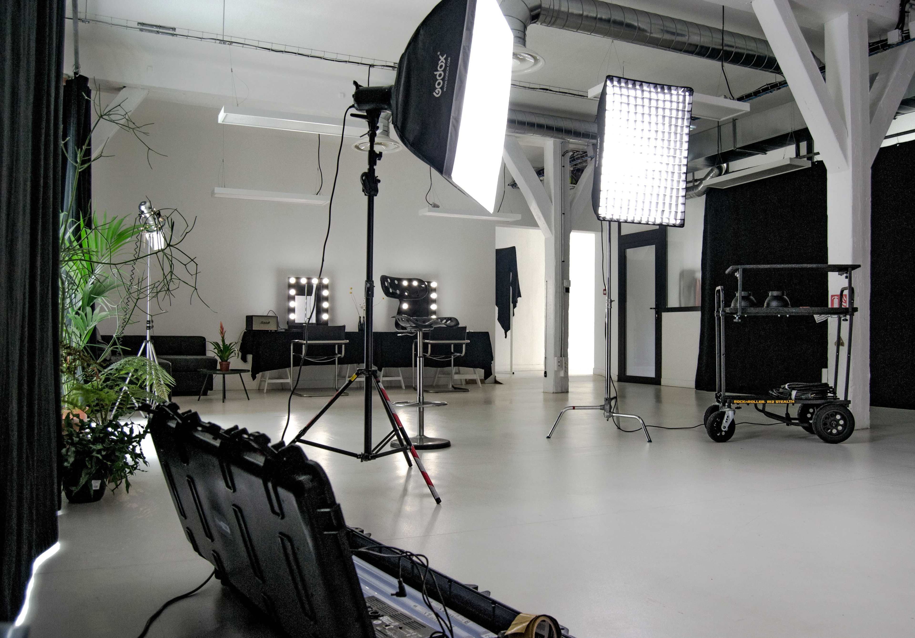 The image shows a photo studio equipped with lighting equipment, mirrors, and a black curtain backdrop, set in a spacious, minimalist room.