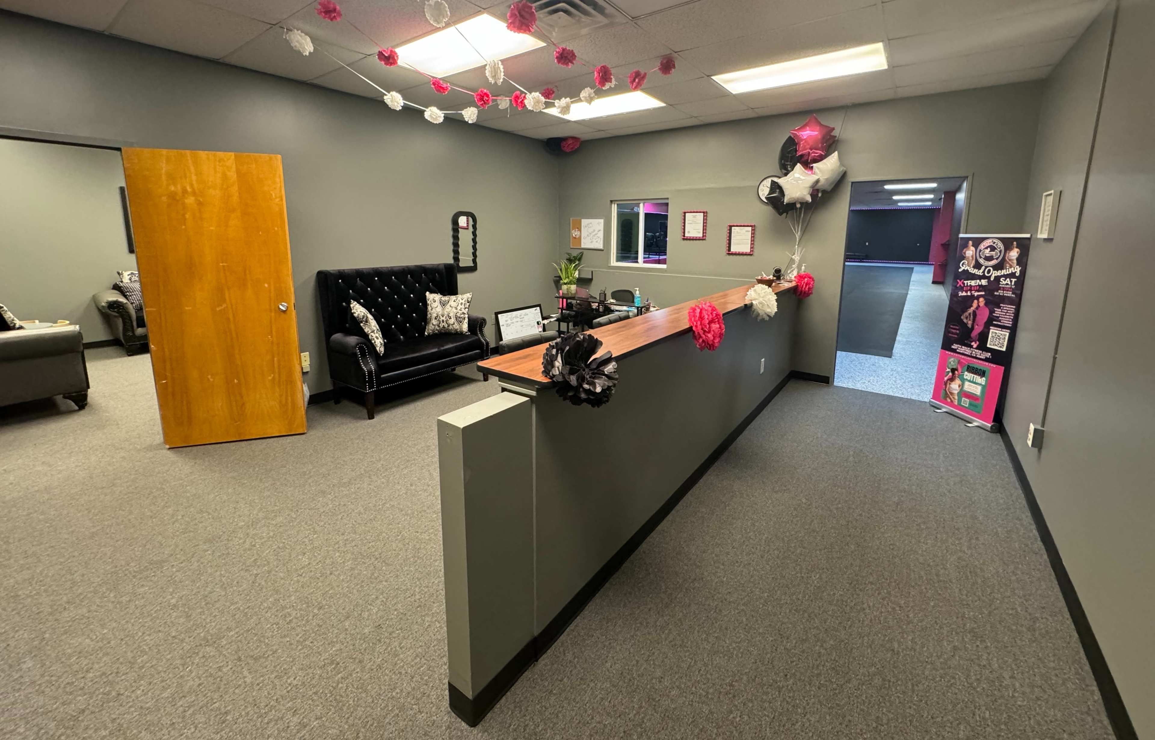 An office reception area with a black couch, a wooden reception desk, and decorated walls featuring pink and black accents.