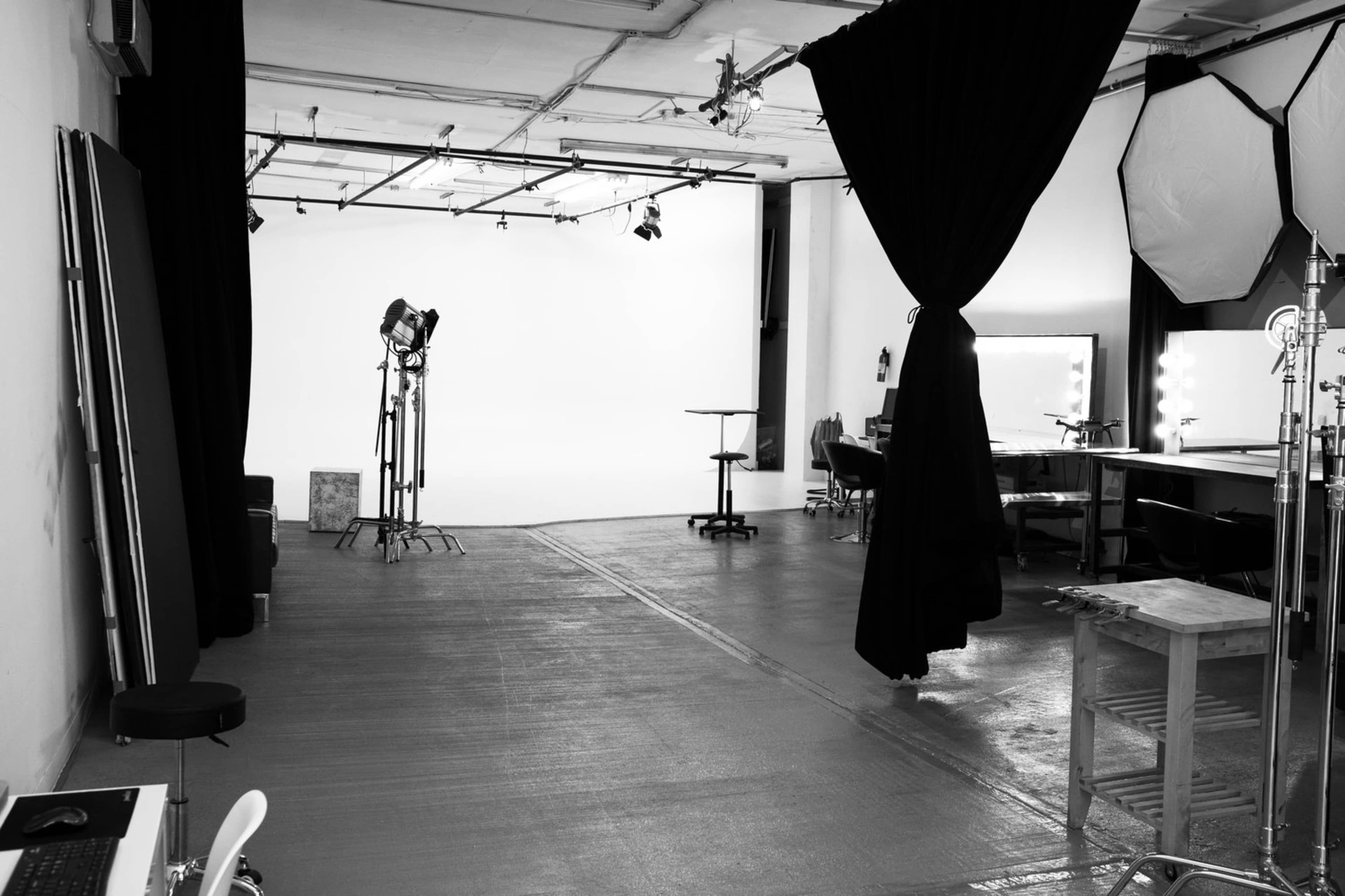 A spacious photography studio with a white backdrop, lighting equipment, and various props arranged along the sides.