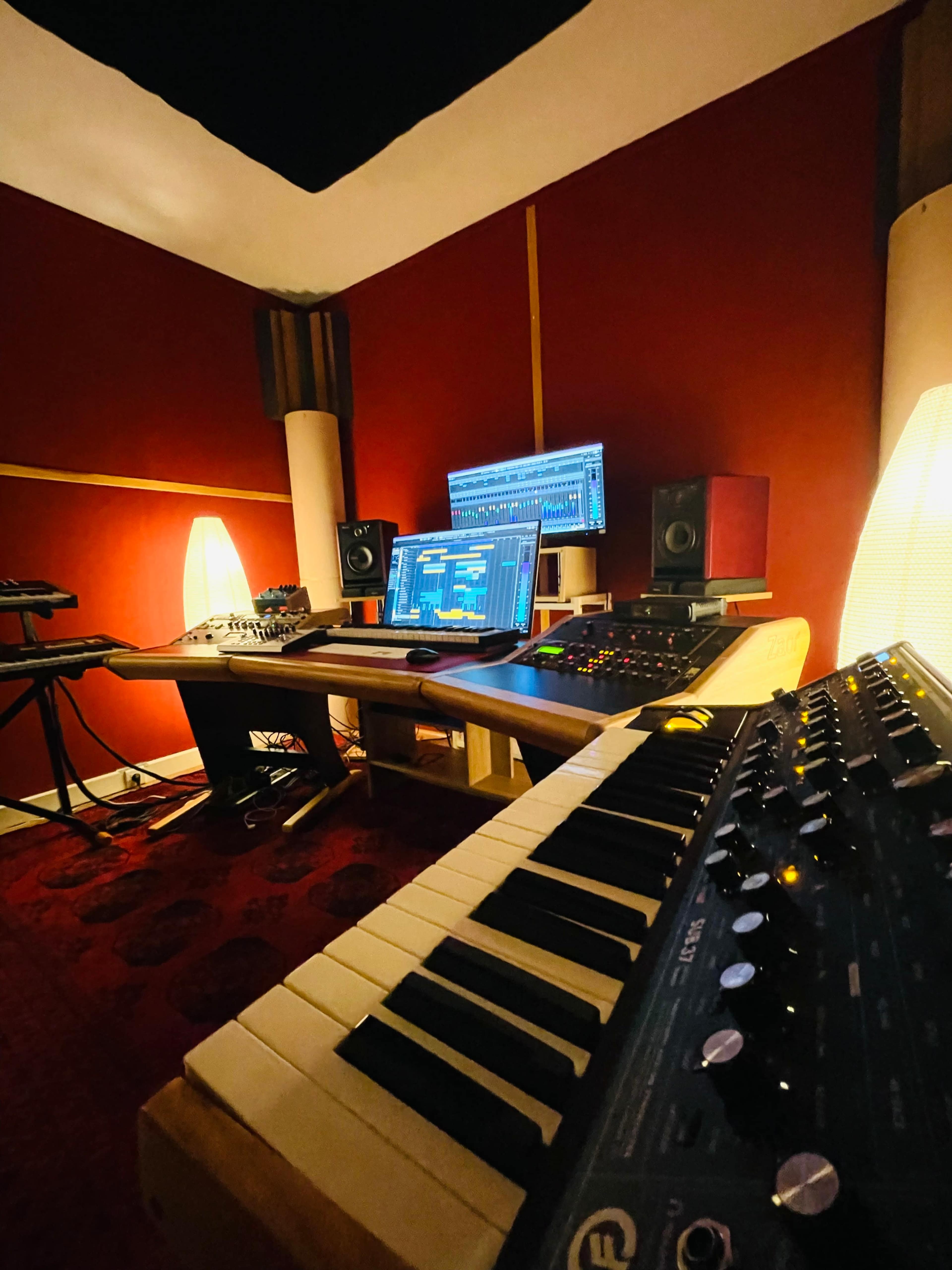 A music production studio with a keyboard, computer screen, speakers, and ambient lighting.