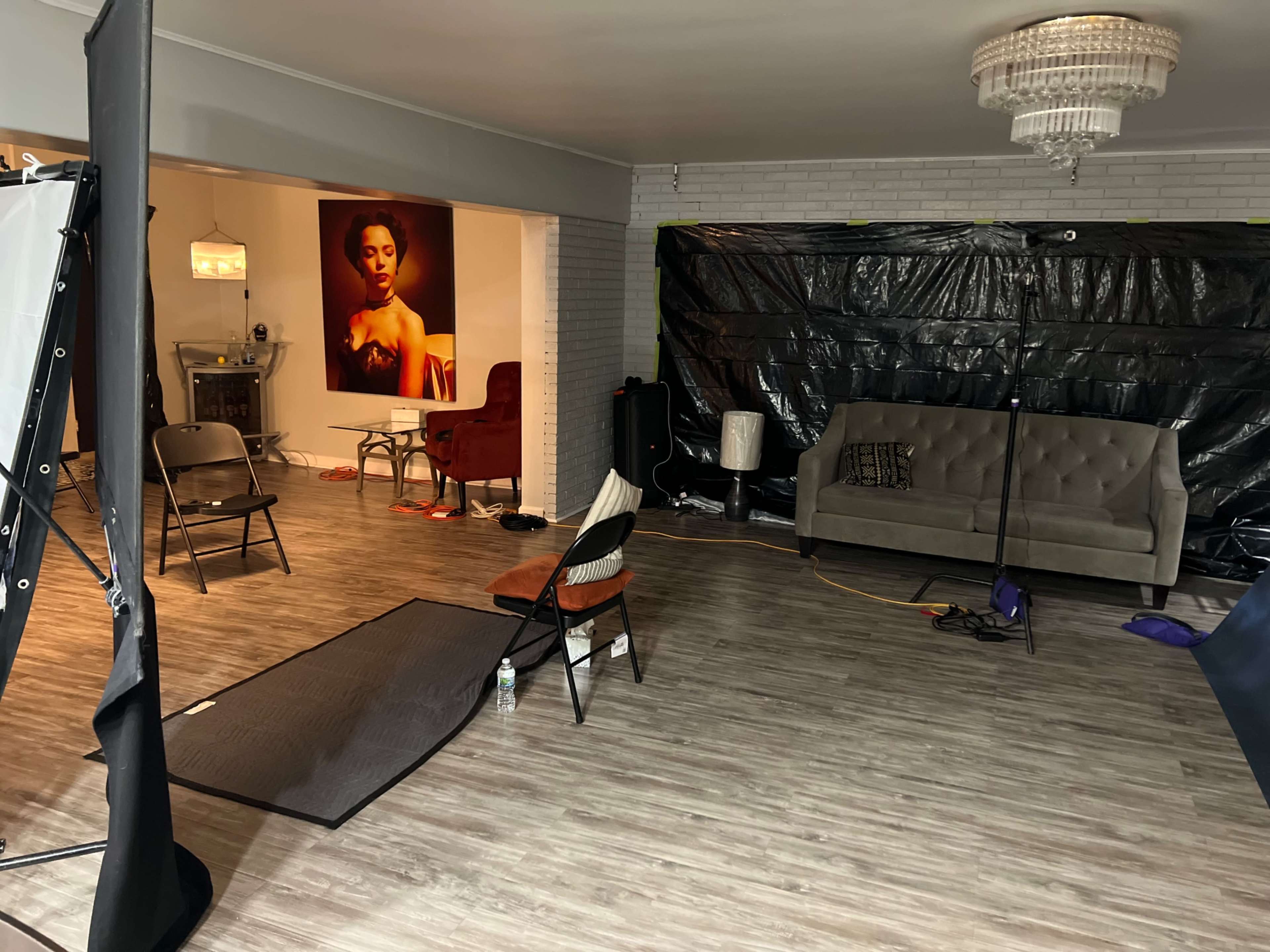 A spacious room features a couch, several chairs, and a large artwork on the wall, with the area partly covered by black plastic sheets.