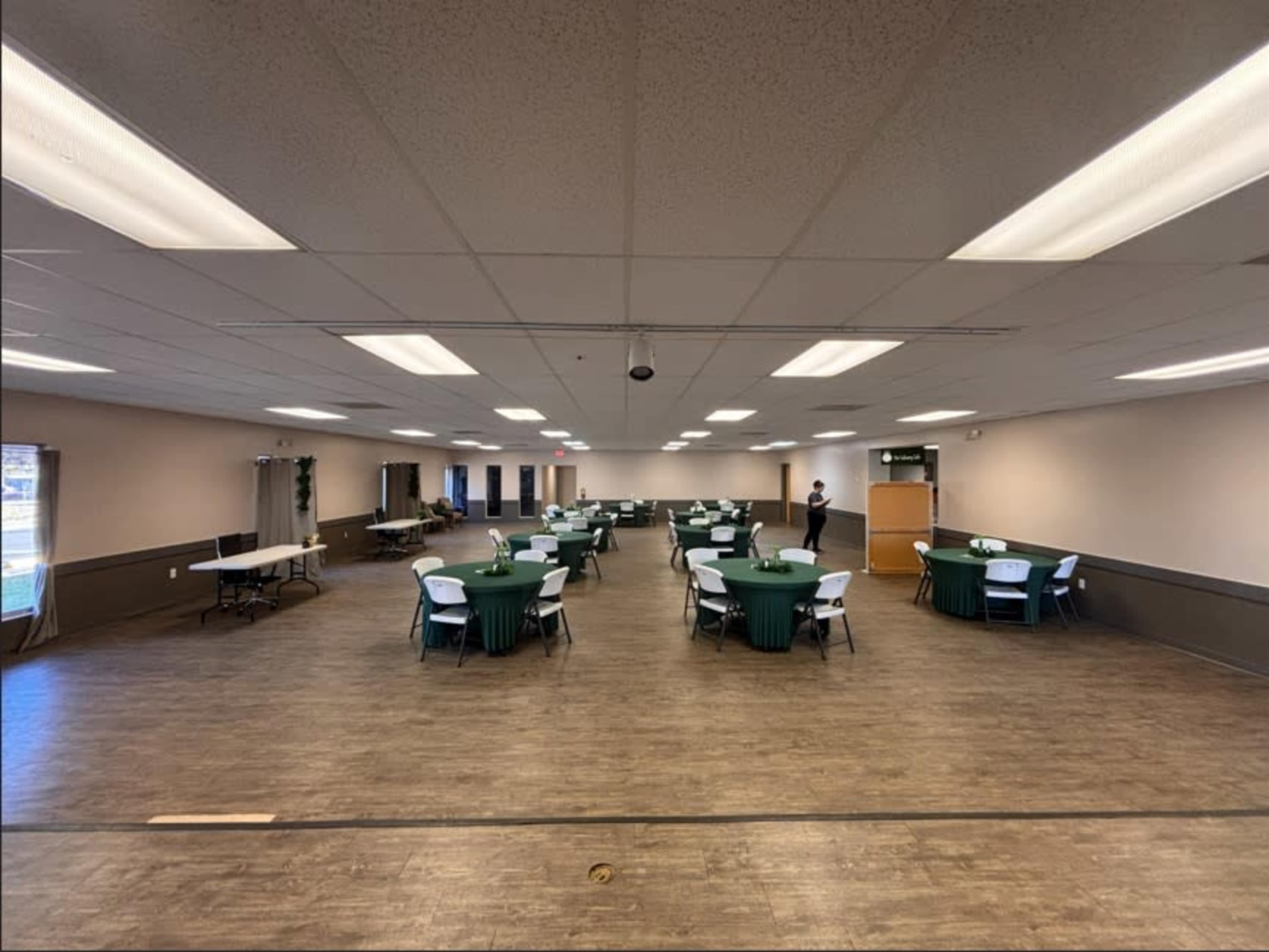 The image shows a spacious event room with several round tables covered in green tablecloths arranged throughout the area.