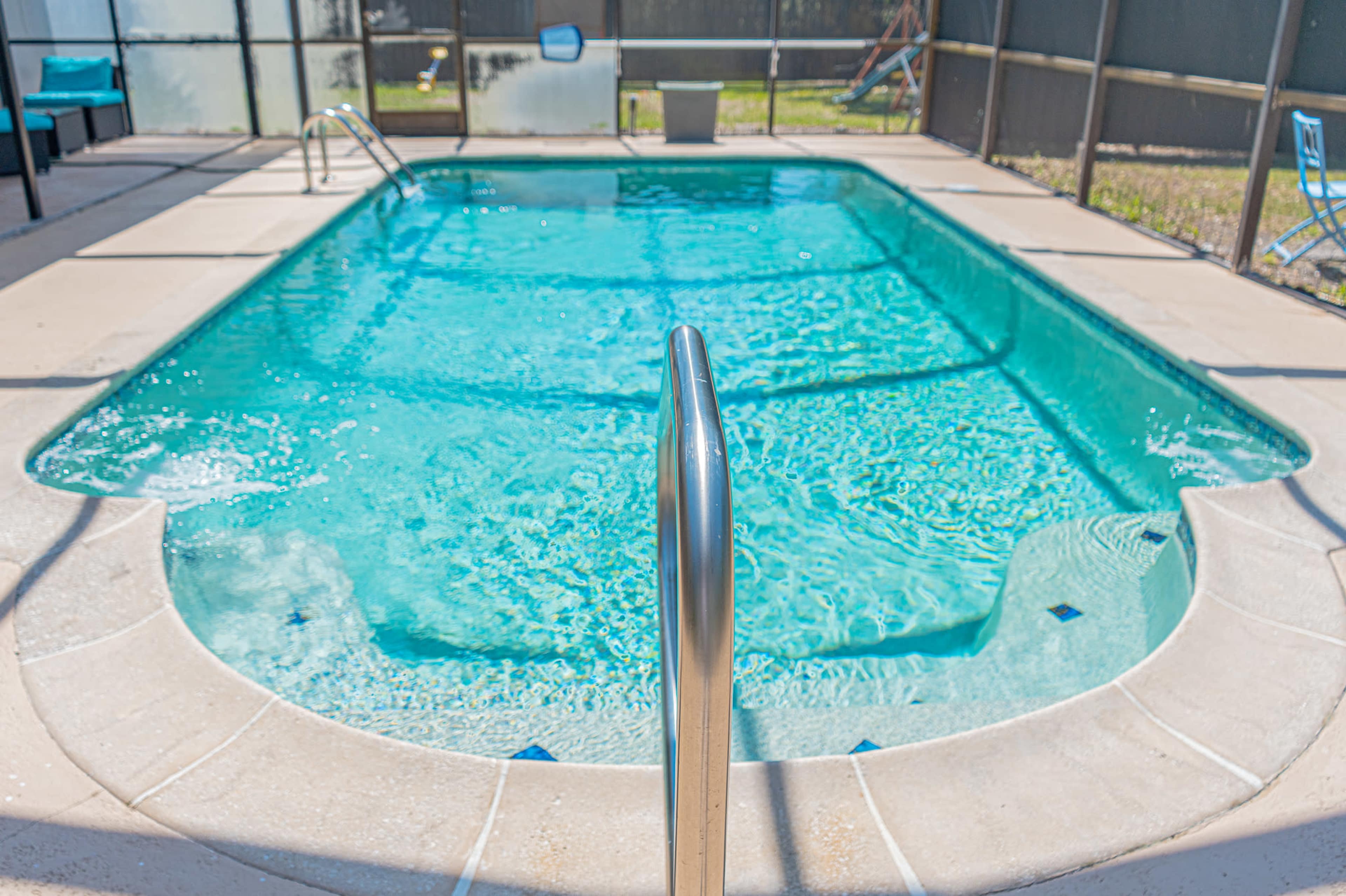 The image shows a clear swimming pool surrounded by a screened enclosure, with a metal ladder leading into the water.