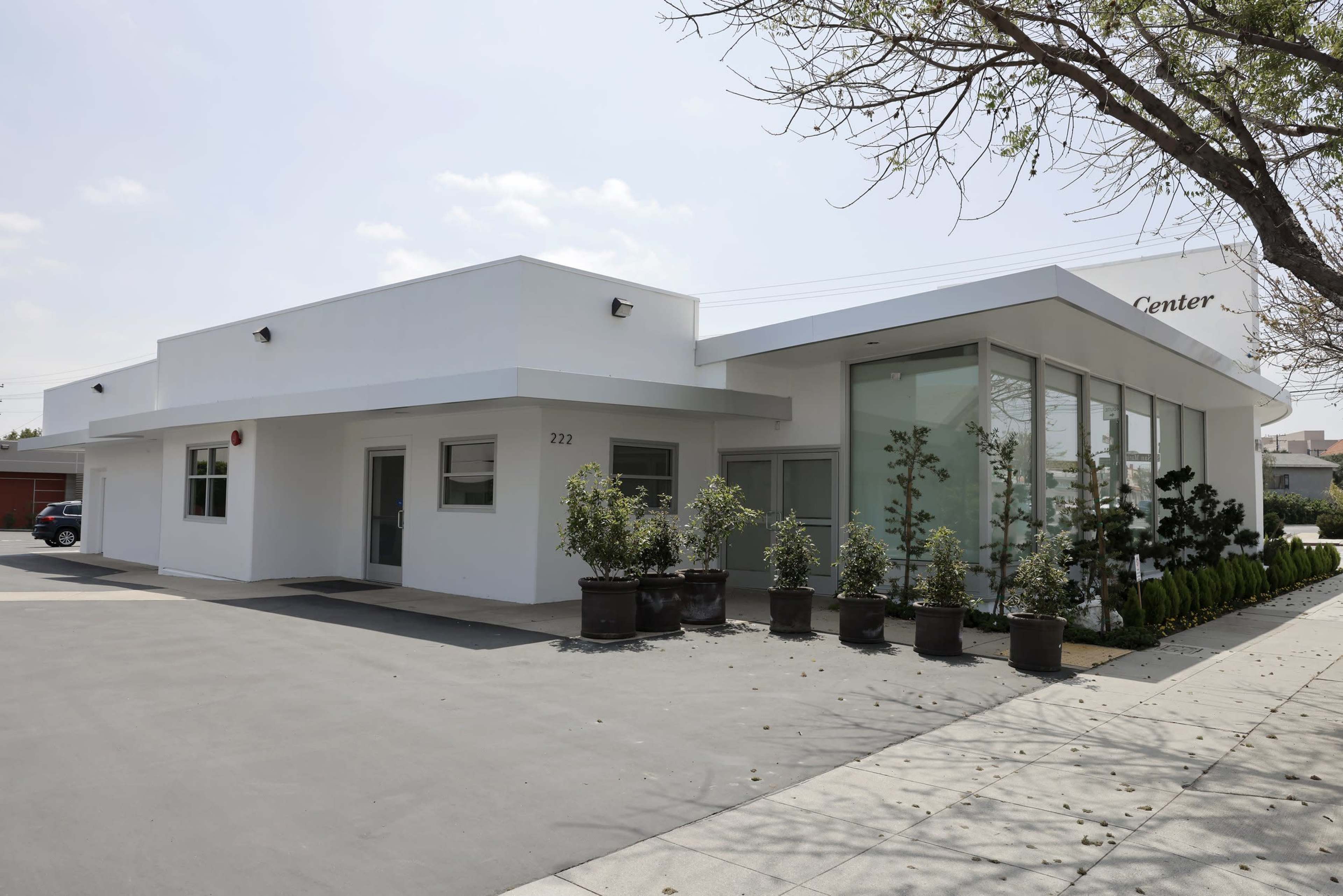 The image shows a modern building with large windows, labeled as a "Center," surrounded by landscaped potted plants and a paved parking area.