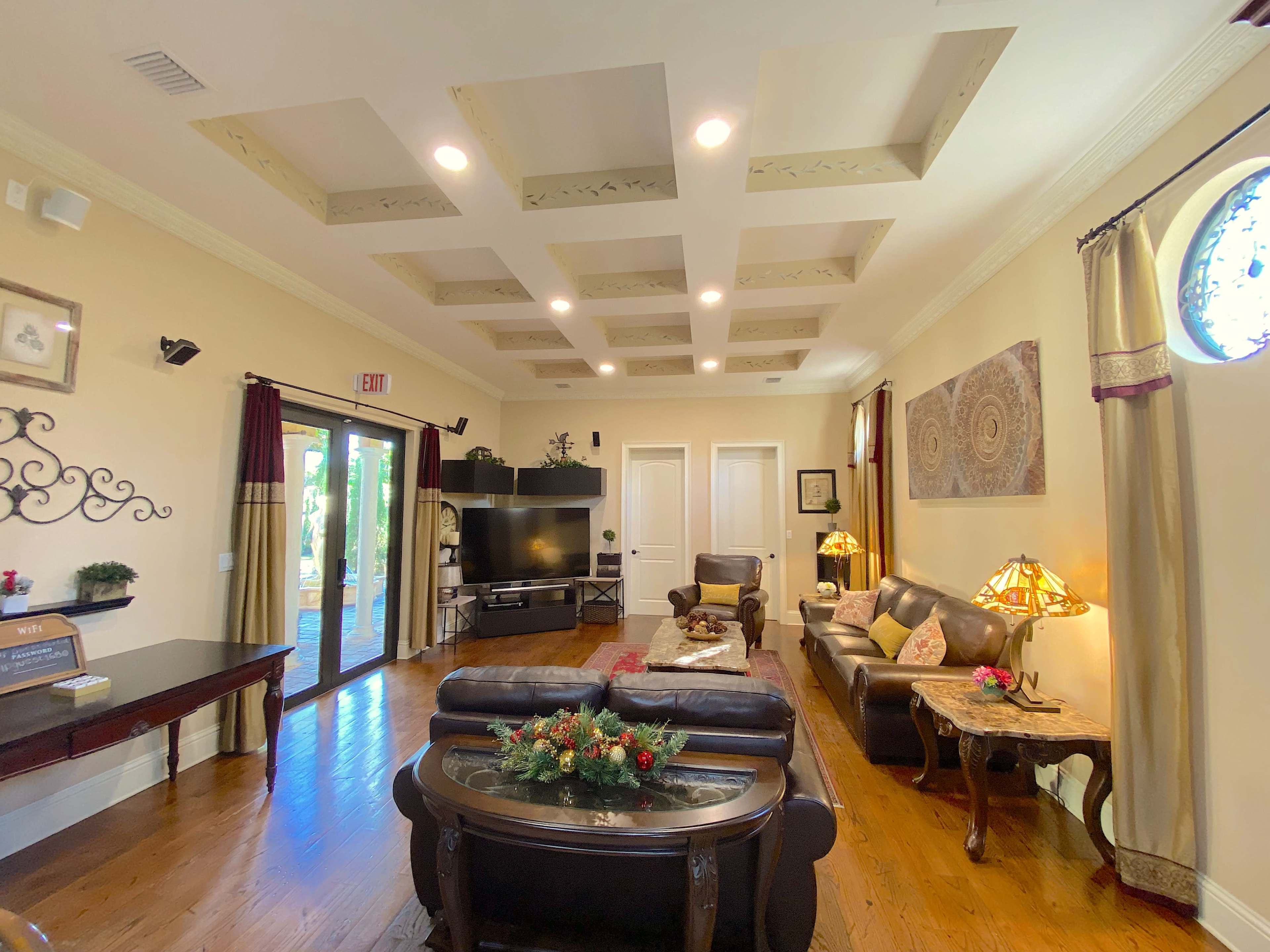 The living room features acoffered ceiling, hardwood flooring, and a mix of comfortable seating arrangements with a television and decorative lighting.
