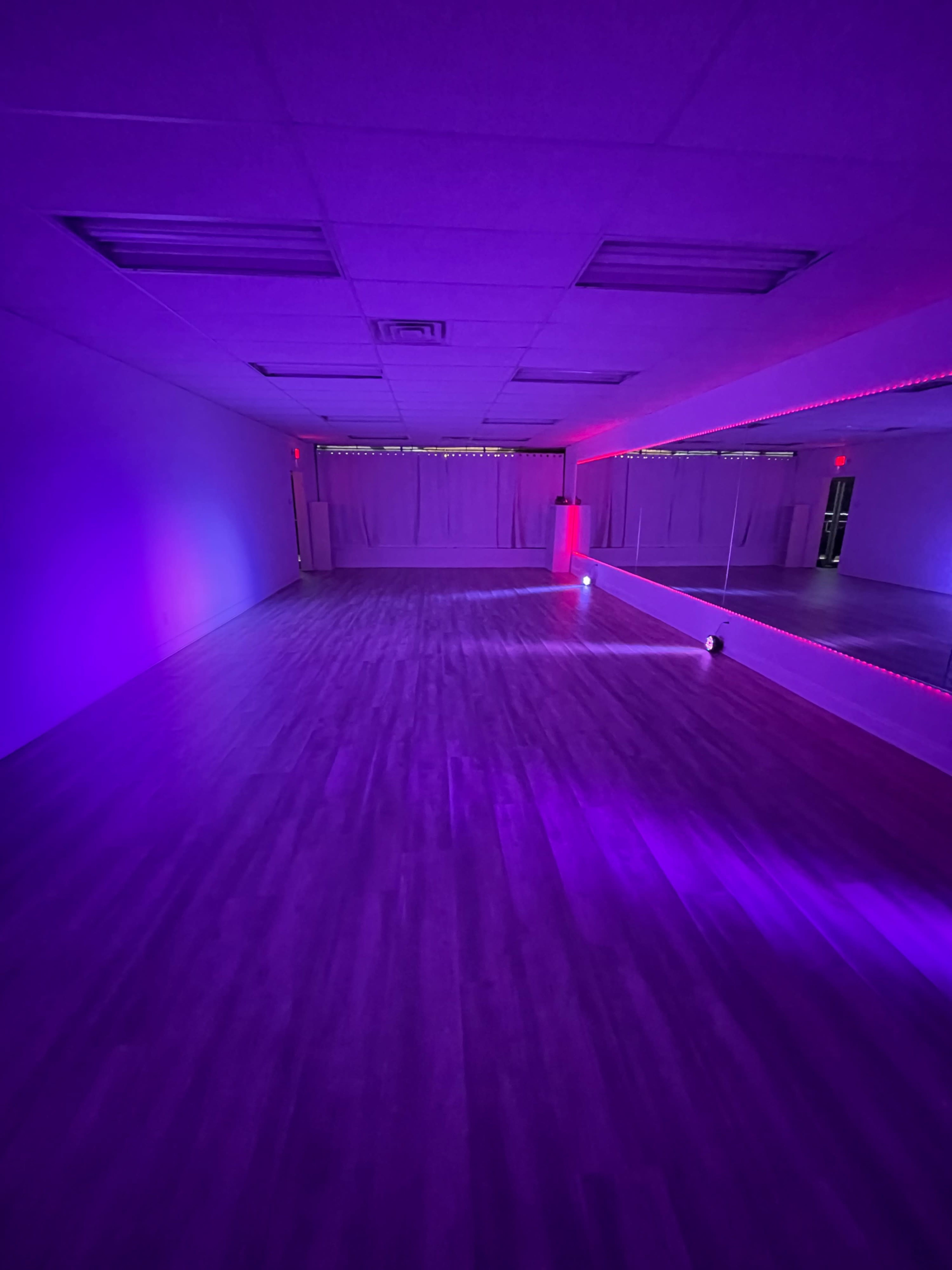 A spacious dance studio with purple lighting and mirrors lining one wall.