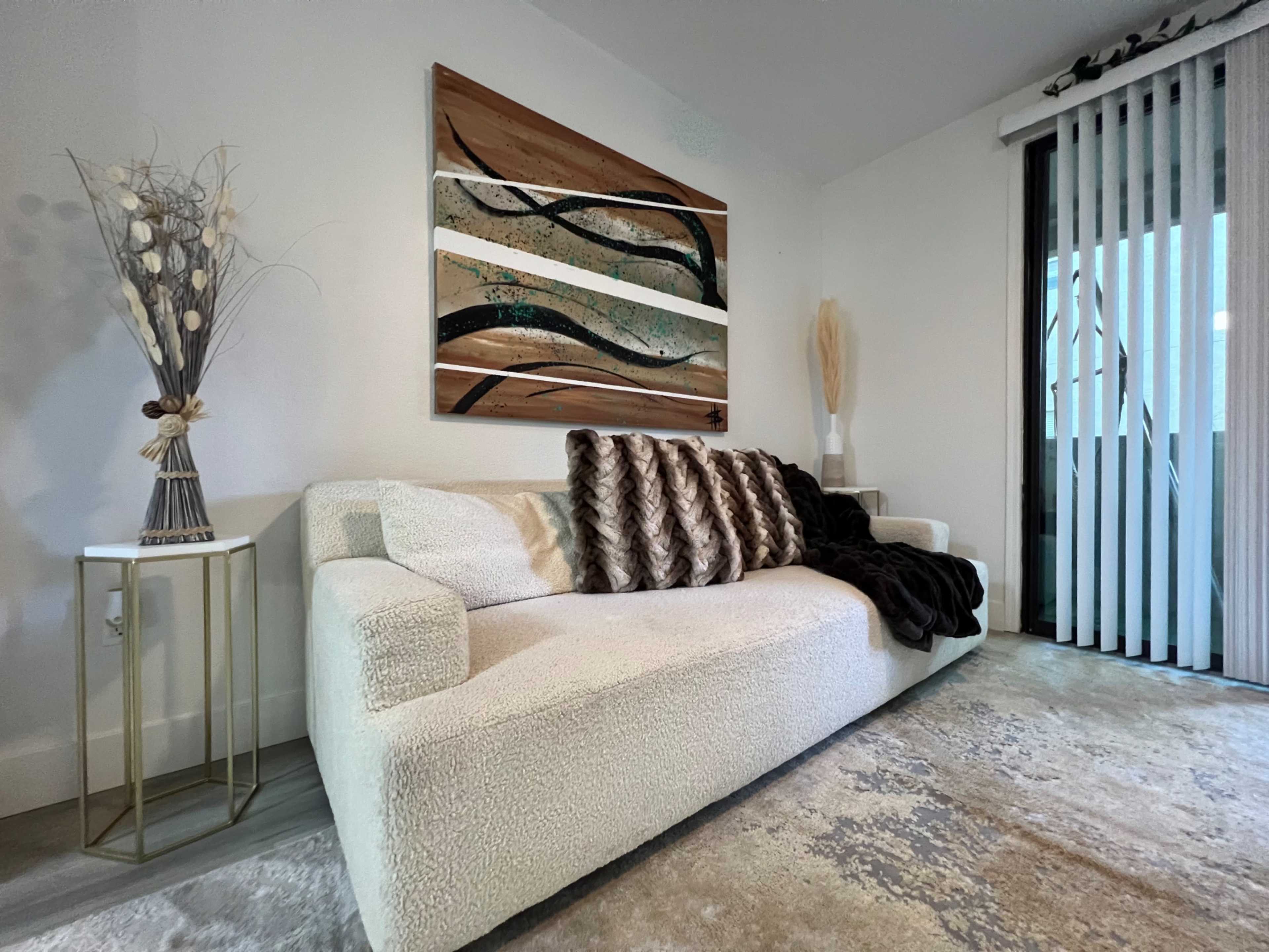 A modern living room with a light-colored sofa, decorative throw pillows, a textured area rug, and a wall-mounted artwork above the couch.